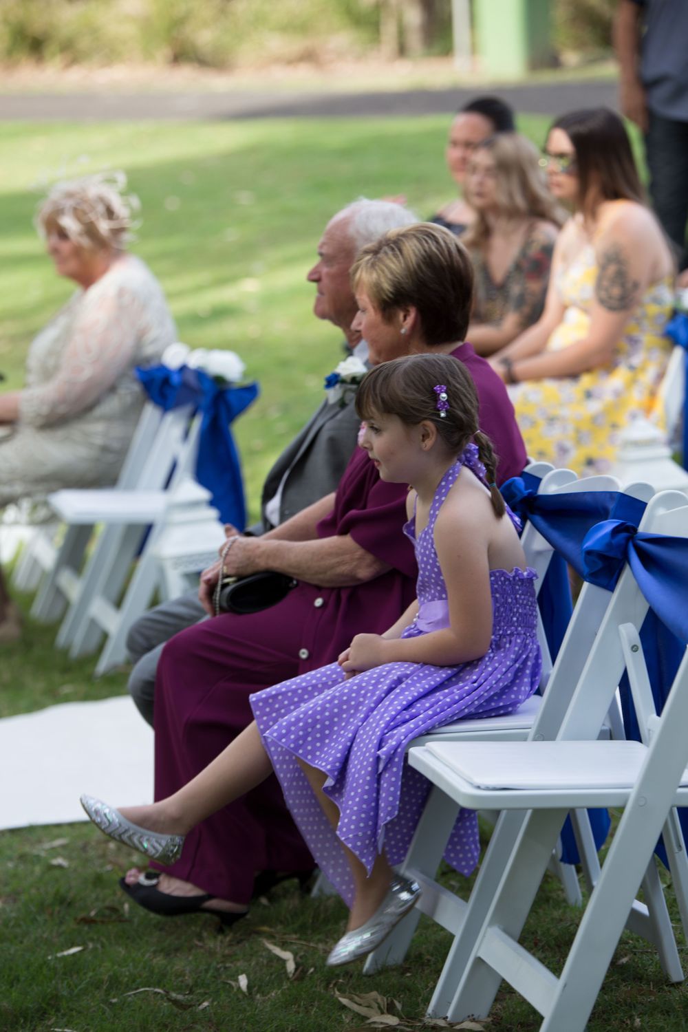 Wedding guests seated in white chairs during an outdoor ceremony.