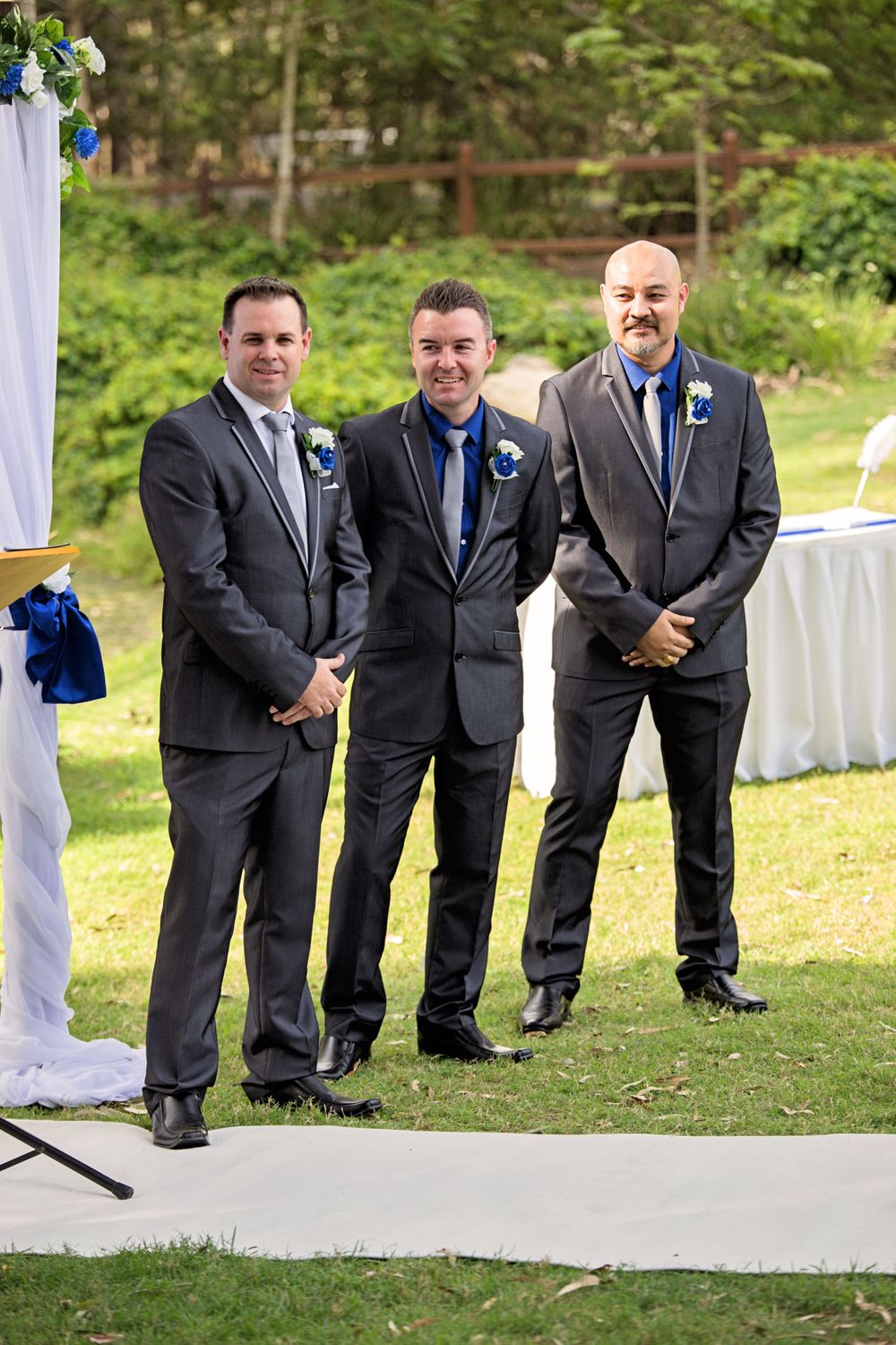 Wedding party in dark suits with blue ties pose together outdoors.