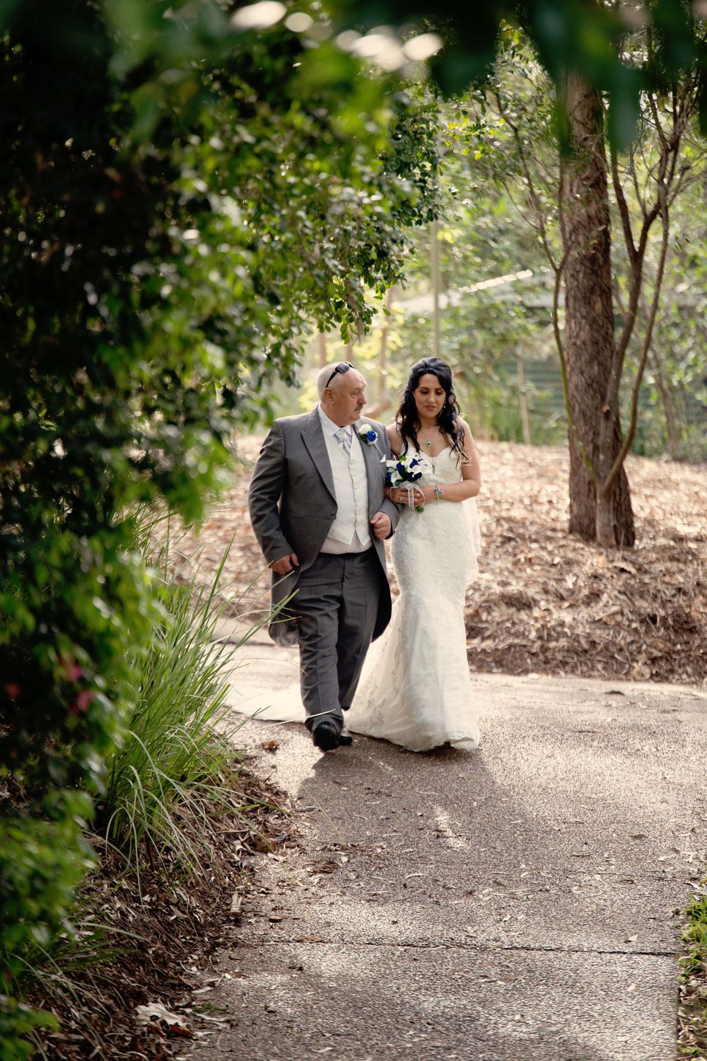A couple walks along a garden path during an outdoor wedding celebration.