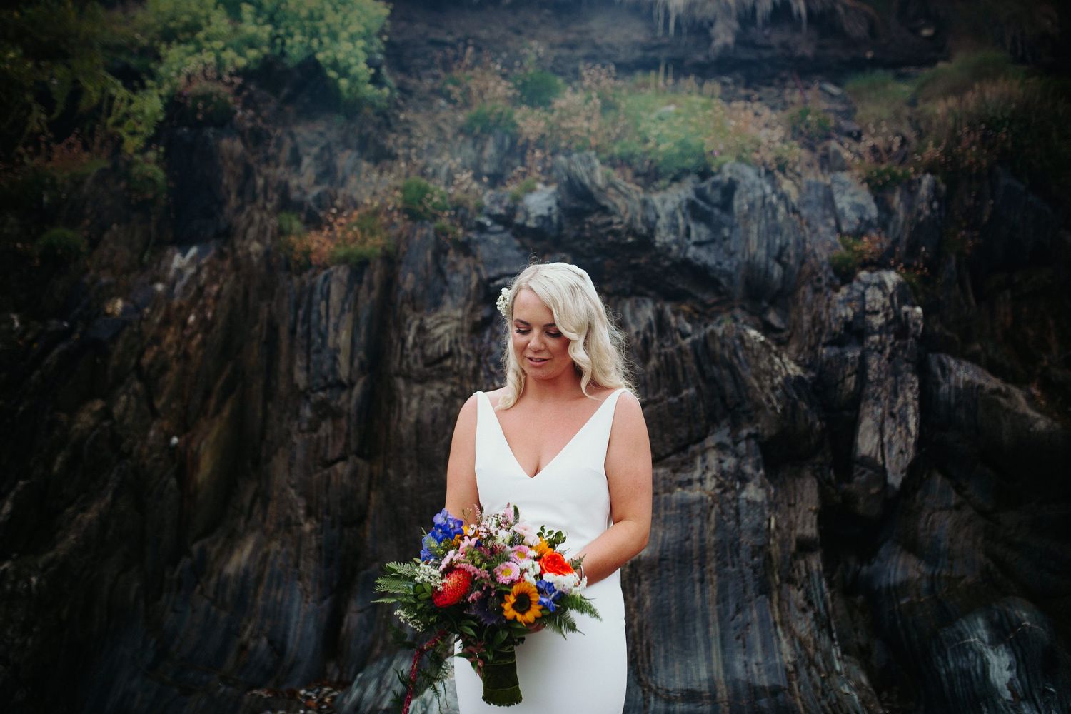 A bride poses with her autumn bouquet against rugged coastal cliffs and rocks.