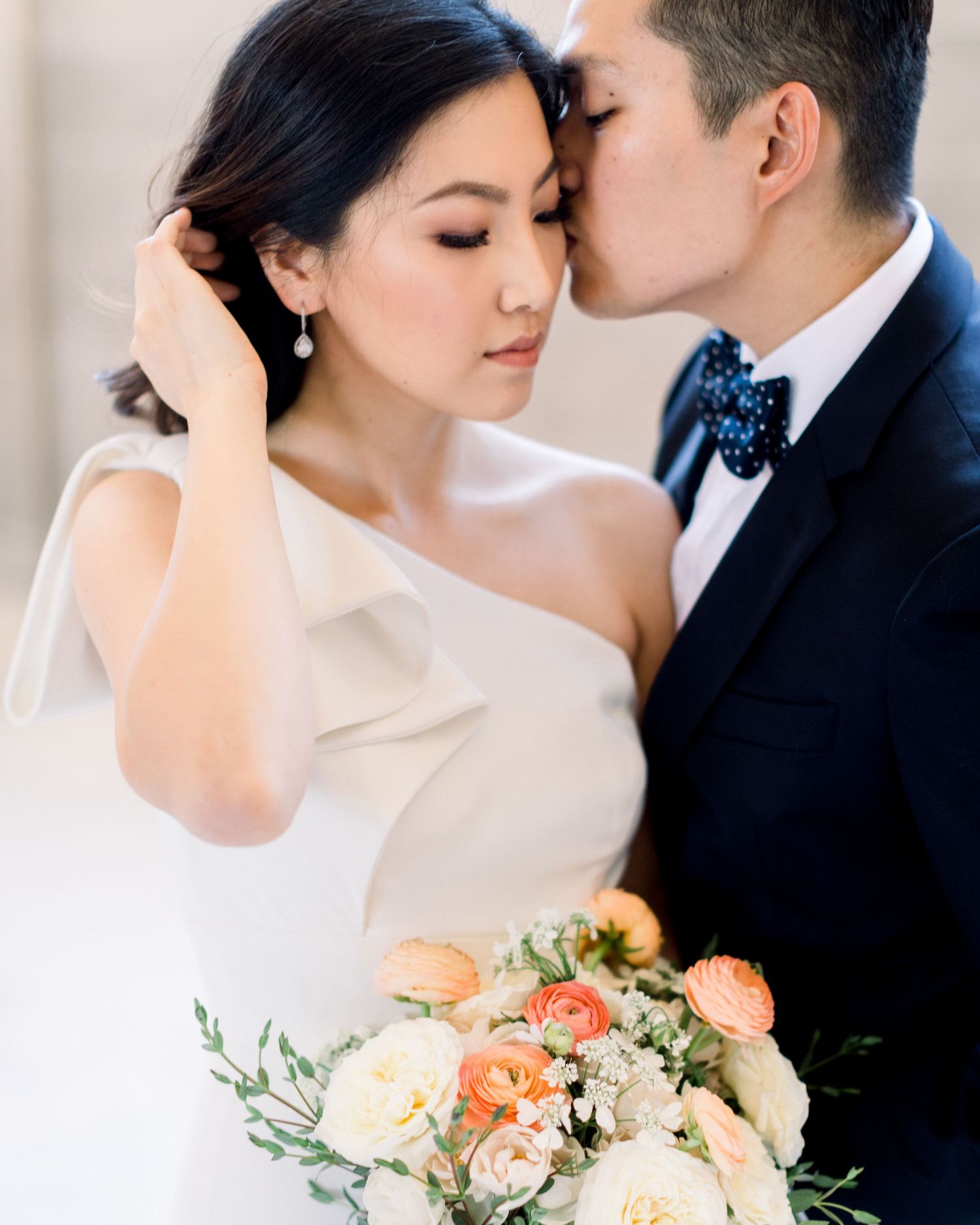 Elegant and sophisticated fine art wedding portrait of a groom kissing the cheek of a bride in a modern gown.