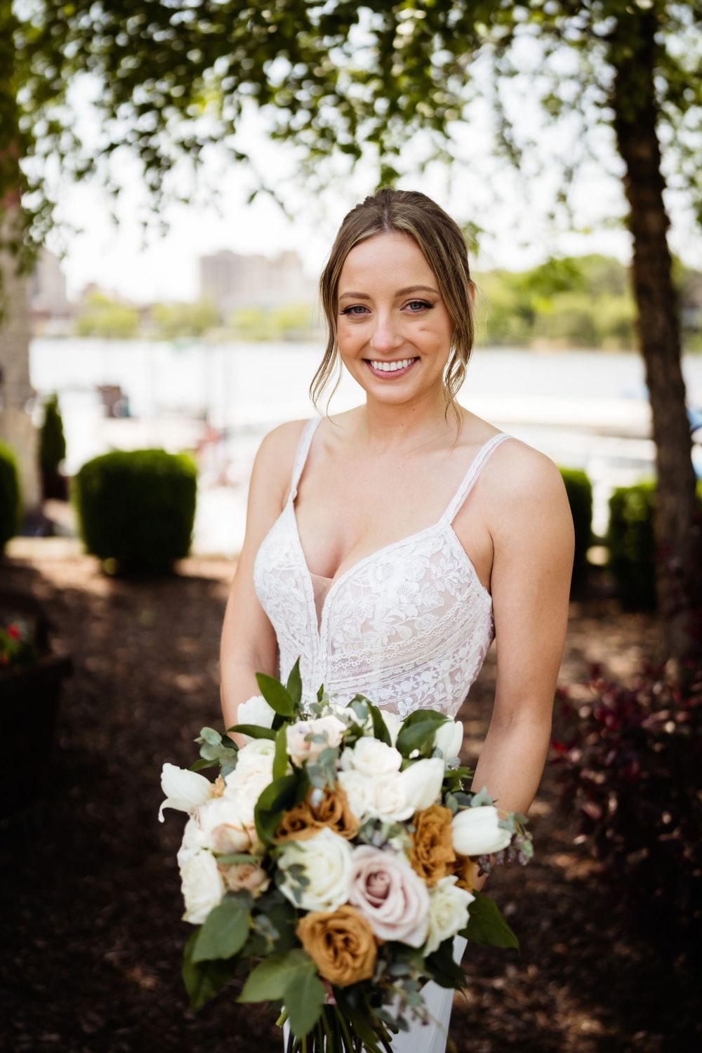 Bride holding bouquet of roses and greenery in outdoor garden setting.