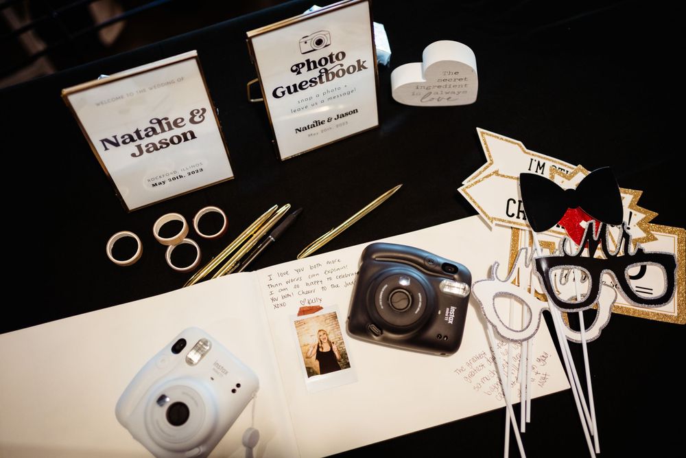 Wedding details including rings, cameras, and props arranged on a white surface.