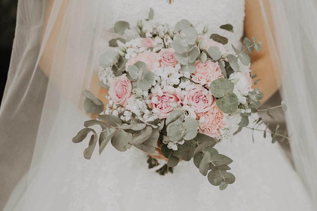 Brud håller i brudbukett med rosa toner. Bröllopsfotografering i Eskilstuna.