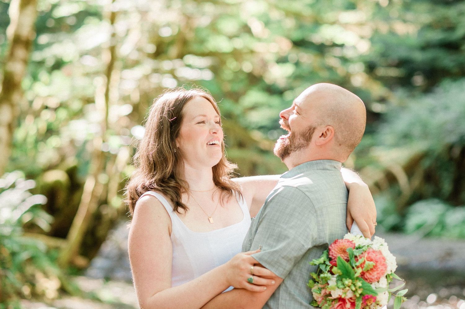 Joyful couple shares candid laughs together in a sunlit forest setting during their Washington elopeemnt.