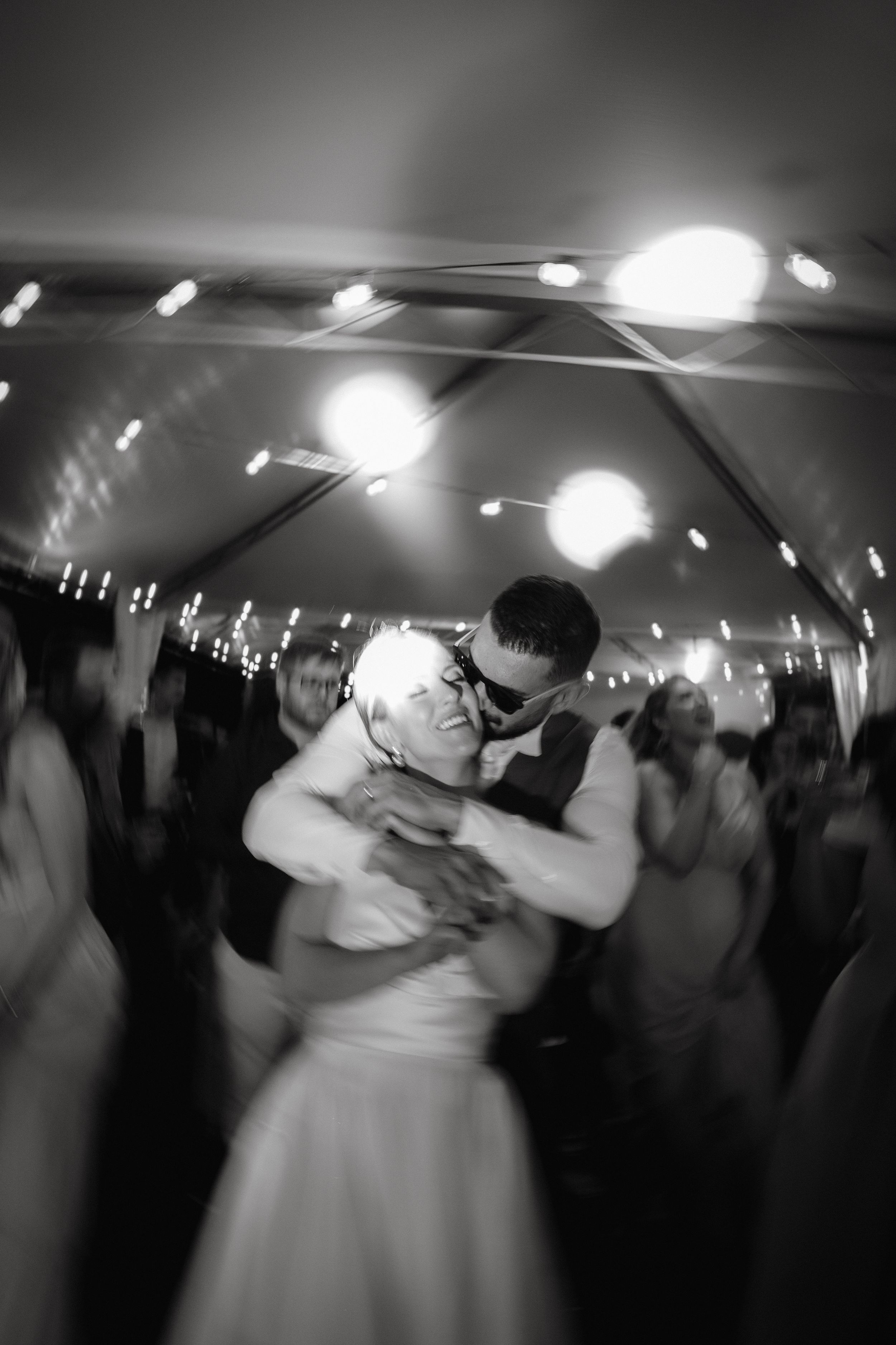 Black and white photo of couple dancing under tent lights at wedding reception.
