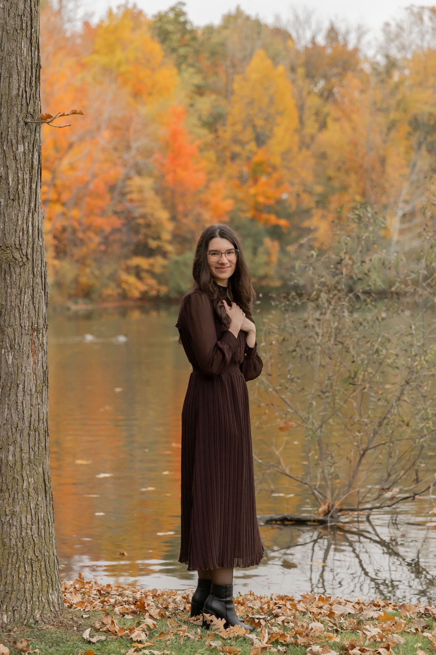 teenage girl in a brown dress posing for a photo in front of a lake in autumn in troy michigan