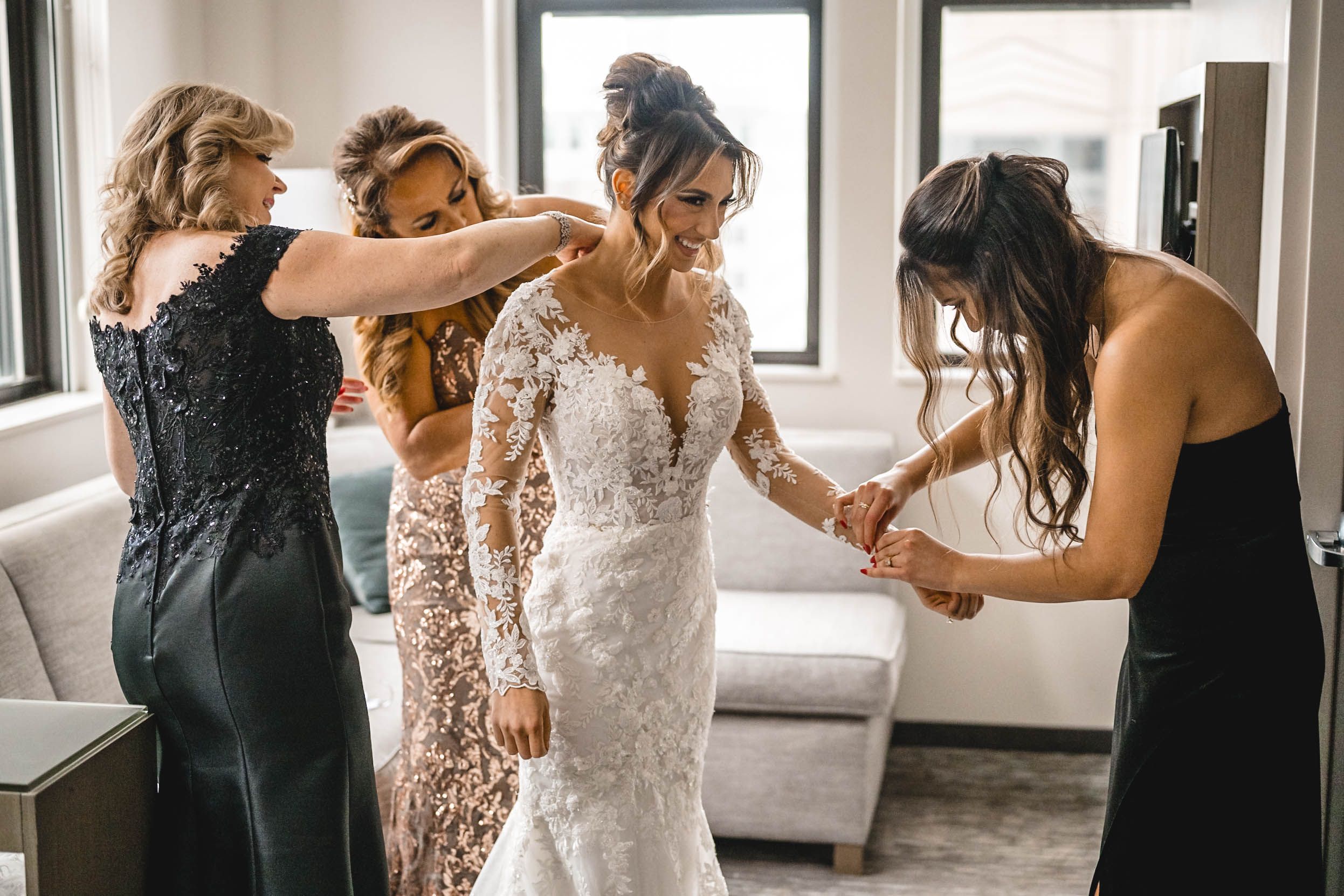 Wedding party shares joyful moment in sunlit room with elegant dresses.