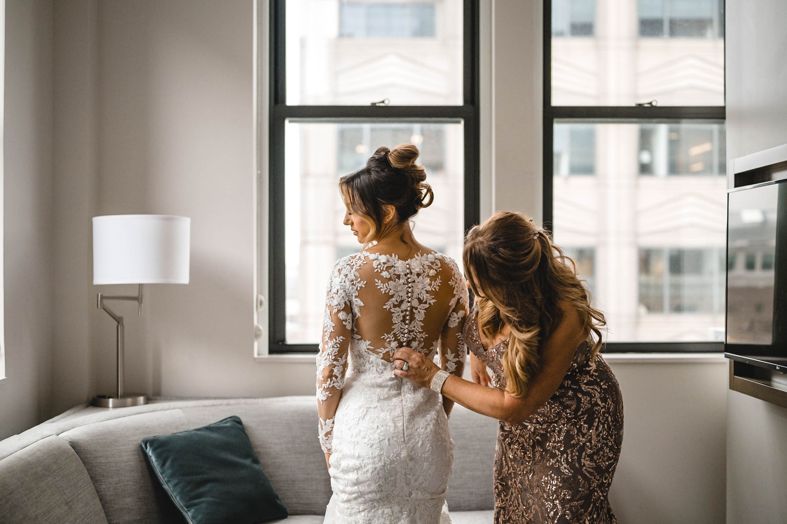 Candid getting ready moment in bright modern room with white wedding dress and sequined gown.