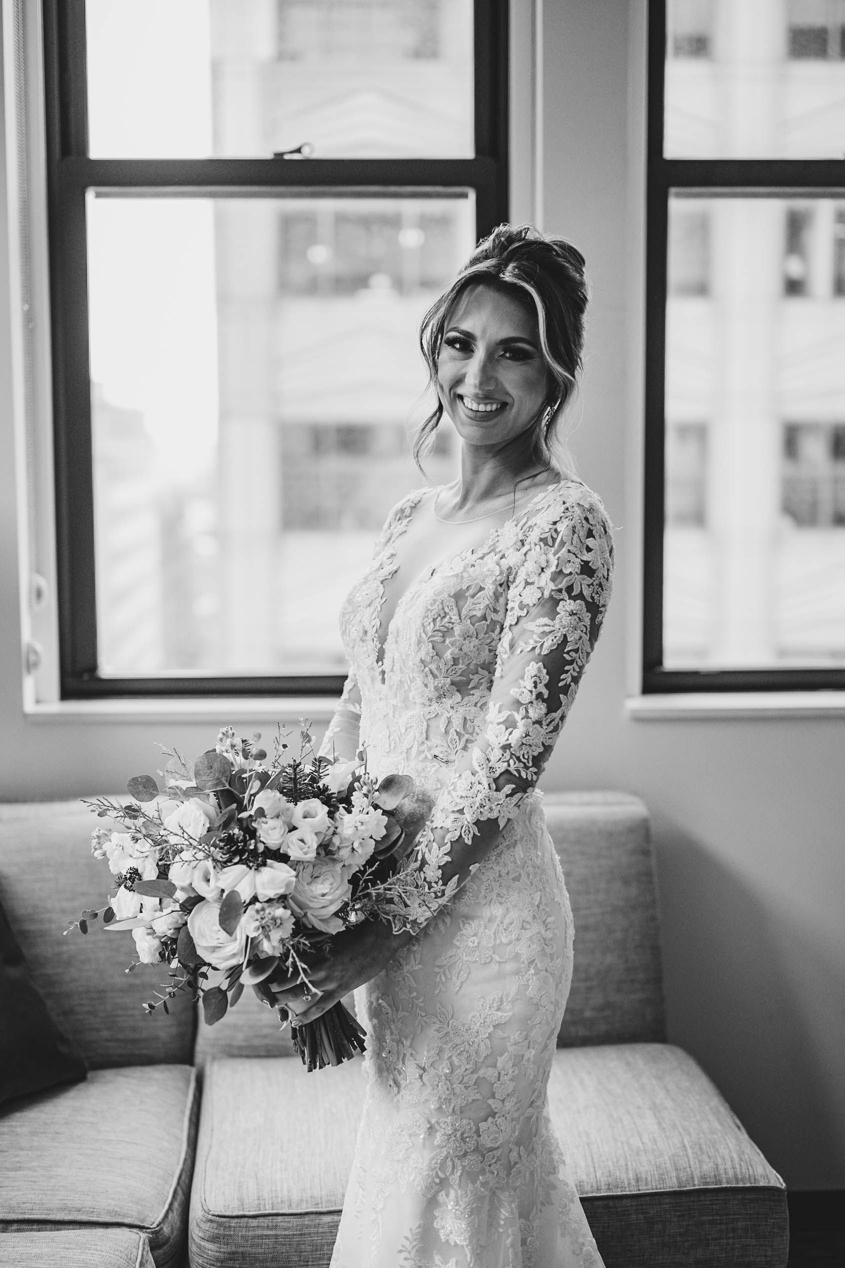 Elegant bridal portrait with lace dress and floral bouquet in modern room.
