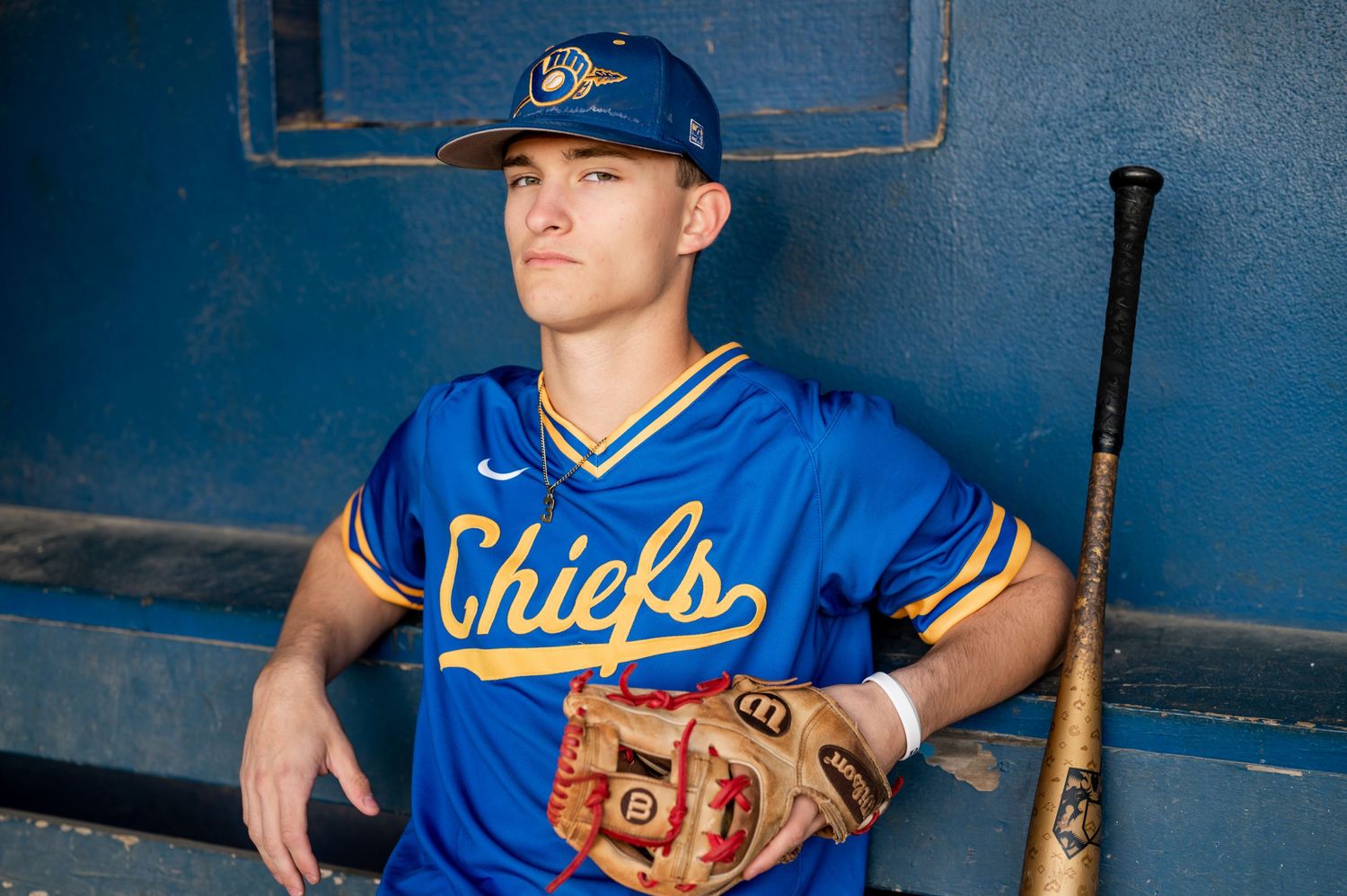 Baseball player in blue Chiefs uniform poses with bat and glove.