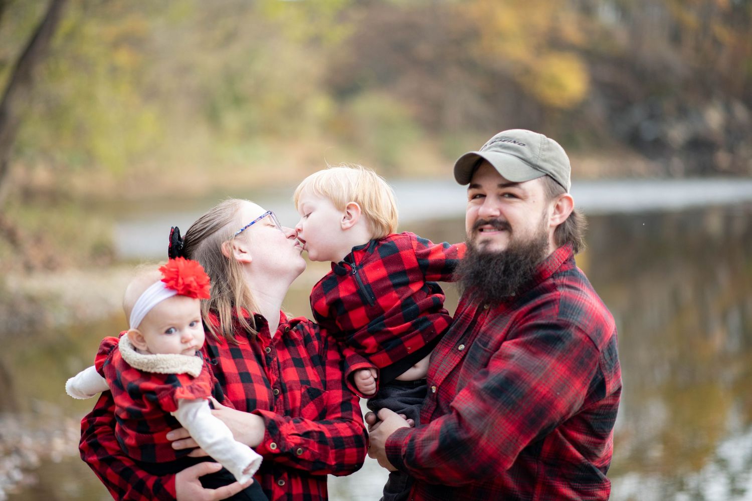Family wearing matching buffalo plaid outfits poses playfully by a lake in autumn.