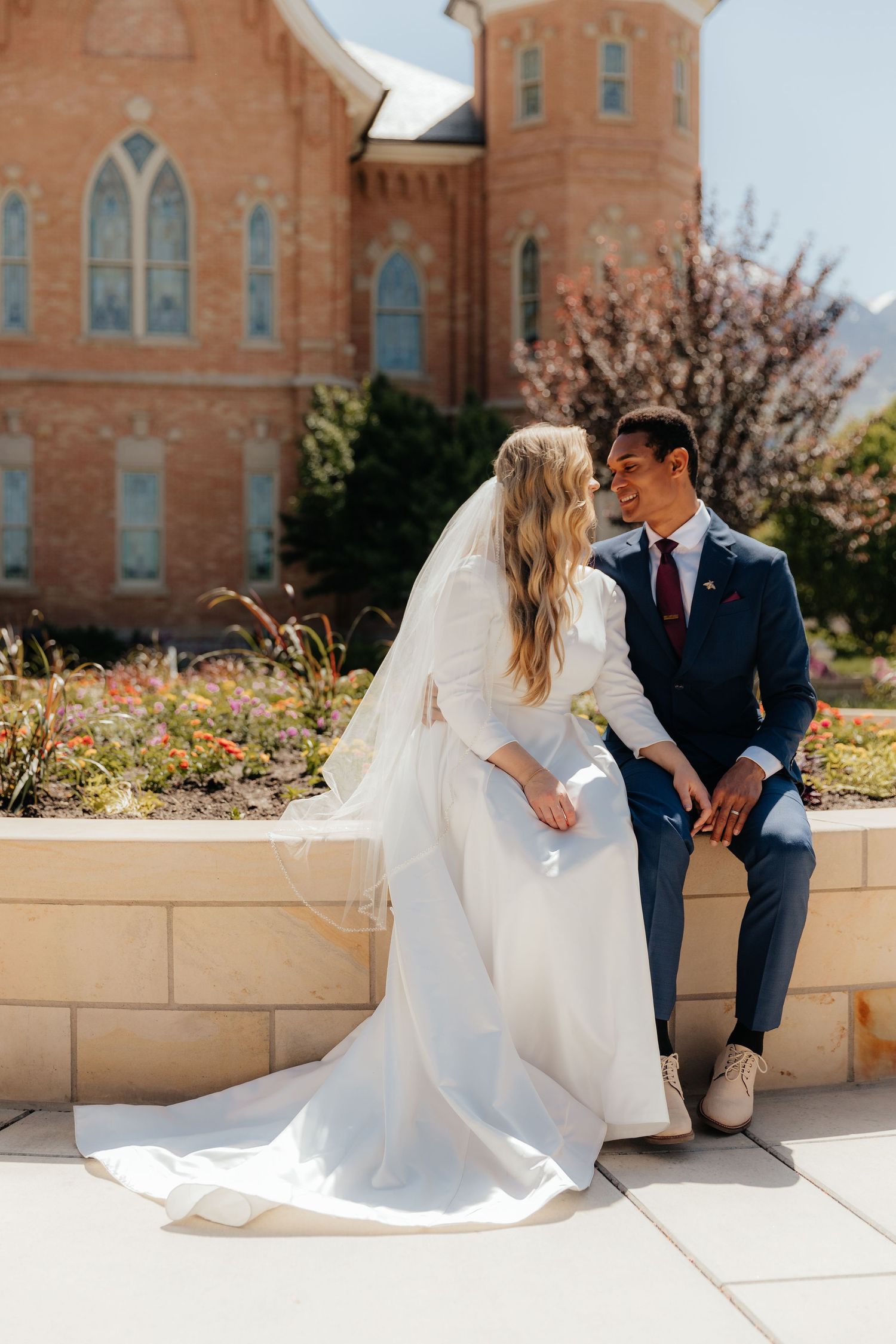 Newly married couple sitting on ledge looking at each other at the Provo City Center LDS Temple