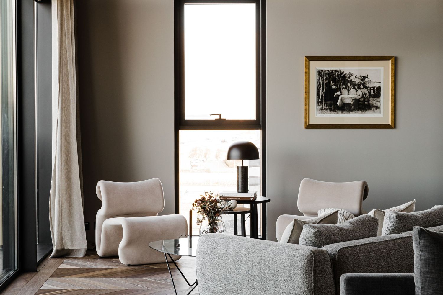 Modern living room with plush chairs, table lamp, and framed artwork in a minimalist gray and white design scheme.