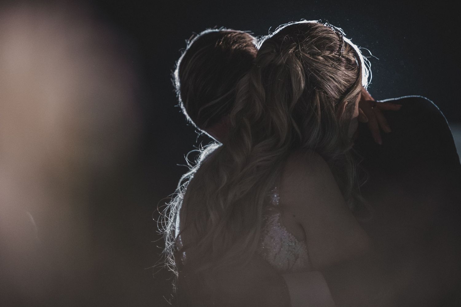 Atmospheric silhouettes of bride and groom embracing in dramatic dark lighting.