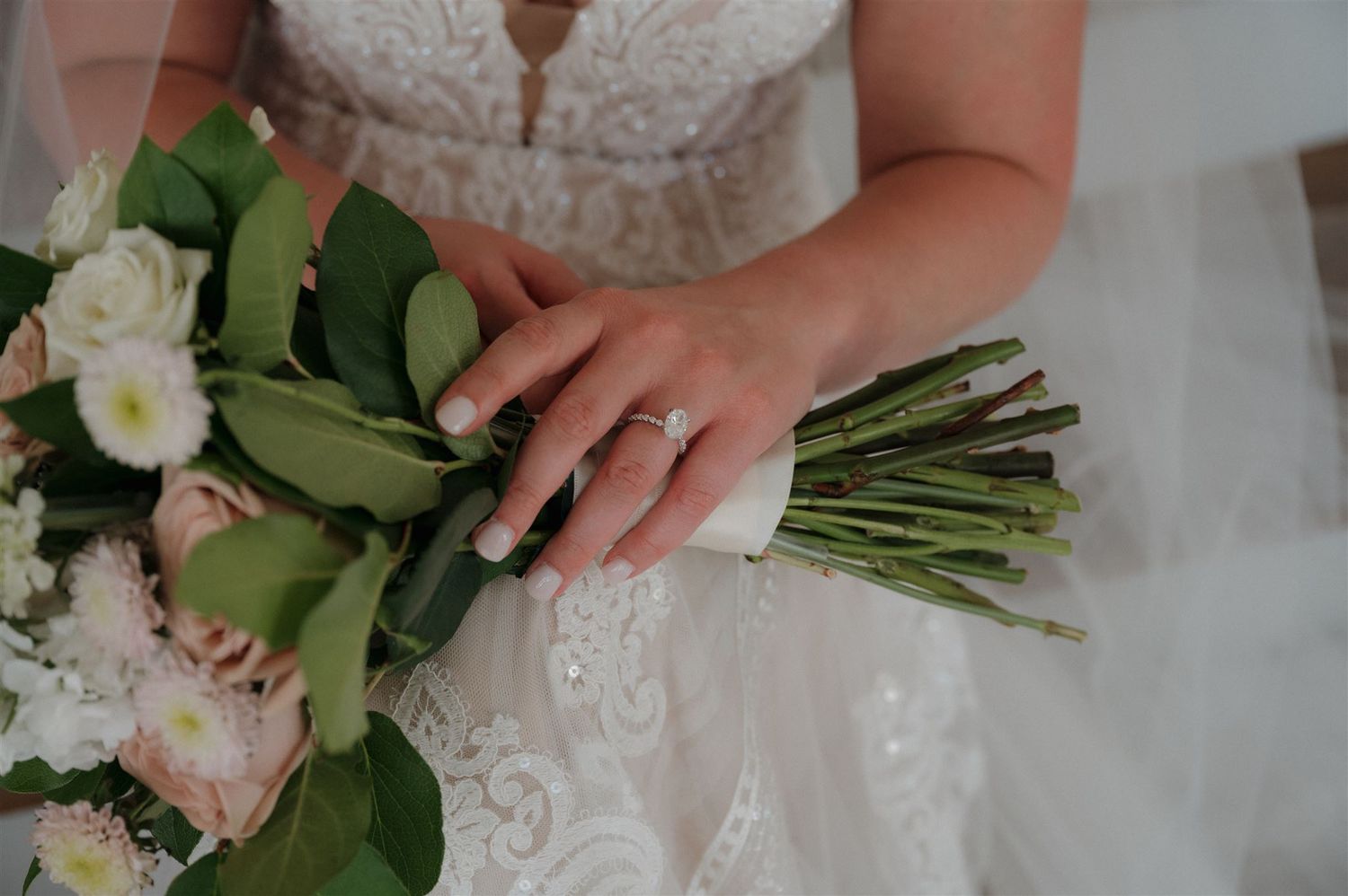 Close-up of bridal bouquet with white roses and greenery held by hands wearing wedding ring.