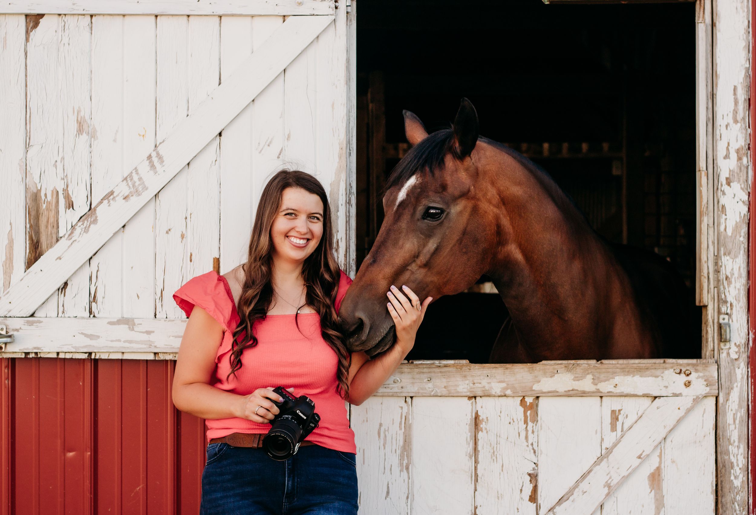 Red barn scene with horse peeking out of stable door.