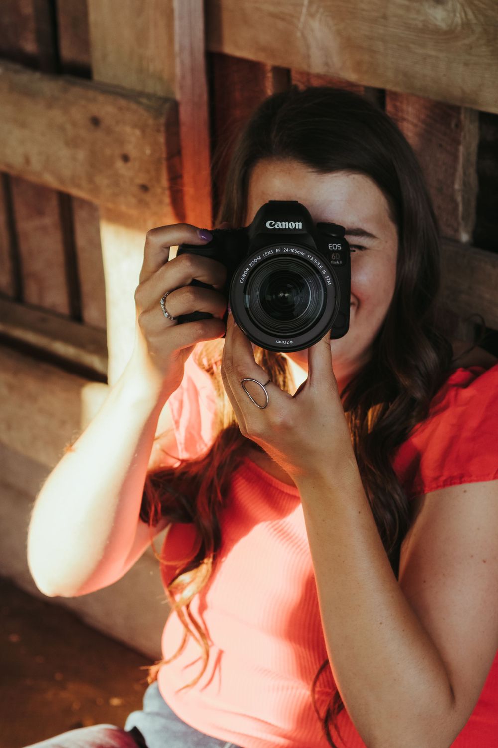 Person holding a Canon DSLR camera in front of their face in warm lighting.
