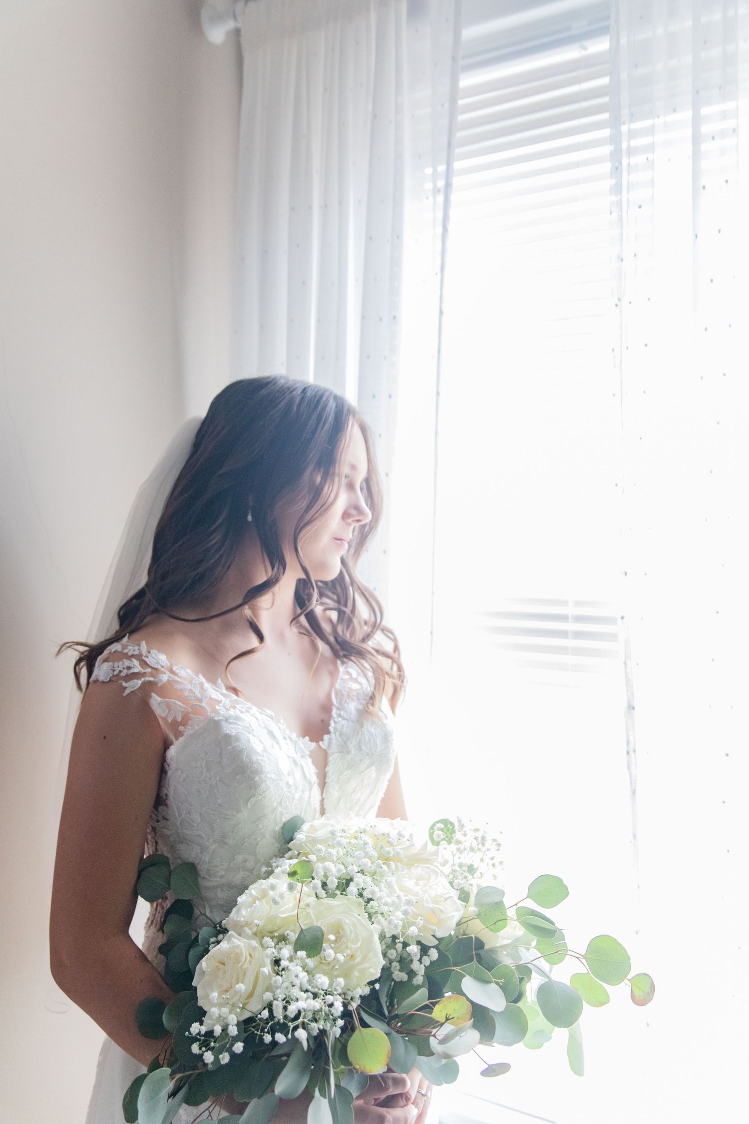 Ethereal window-lit bridal portrait featuring a white bouquet with eucalyptus.