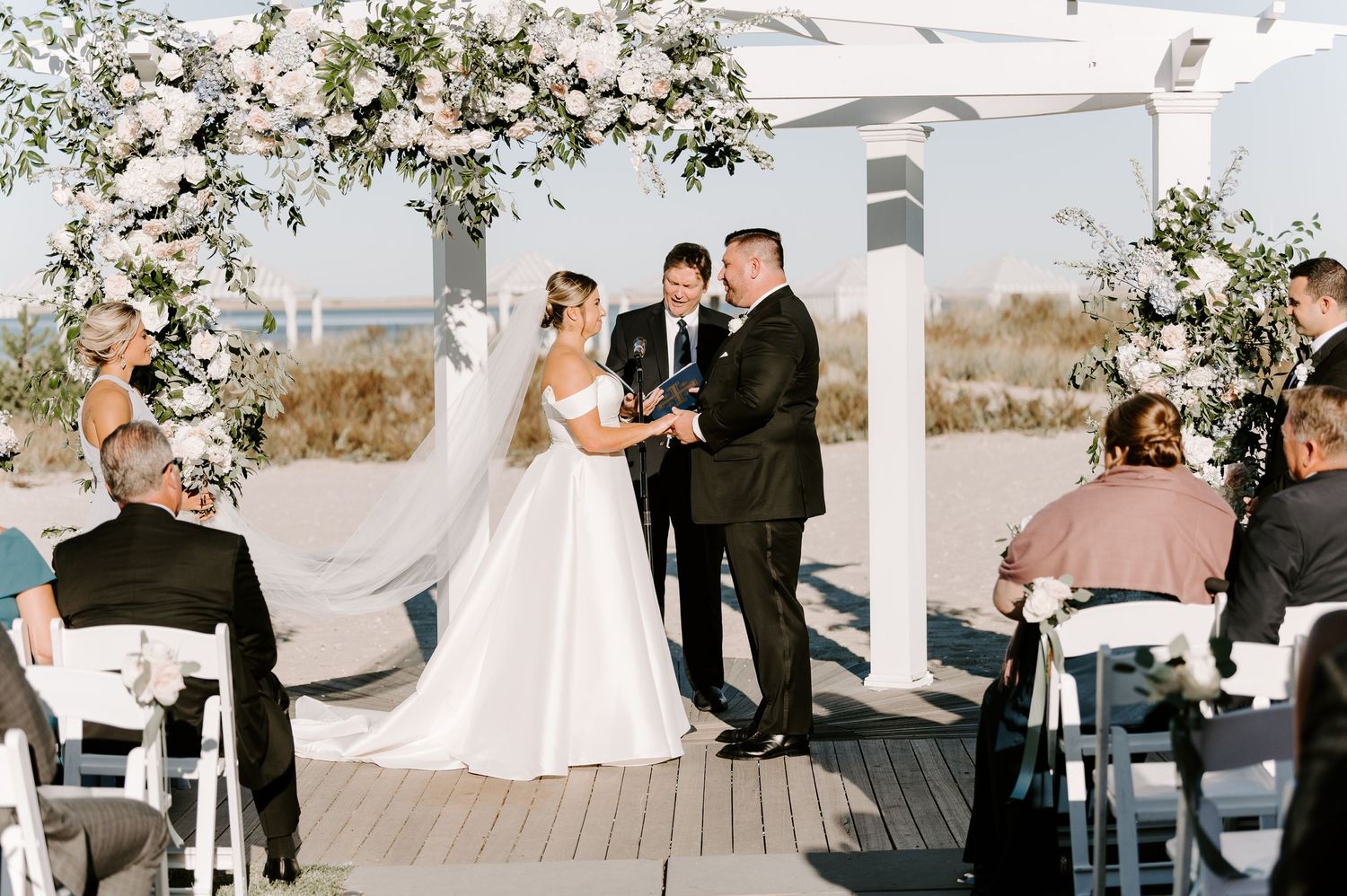 A romantic beach wedding ceremony with white floral arches and ocean views.