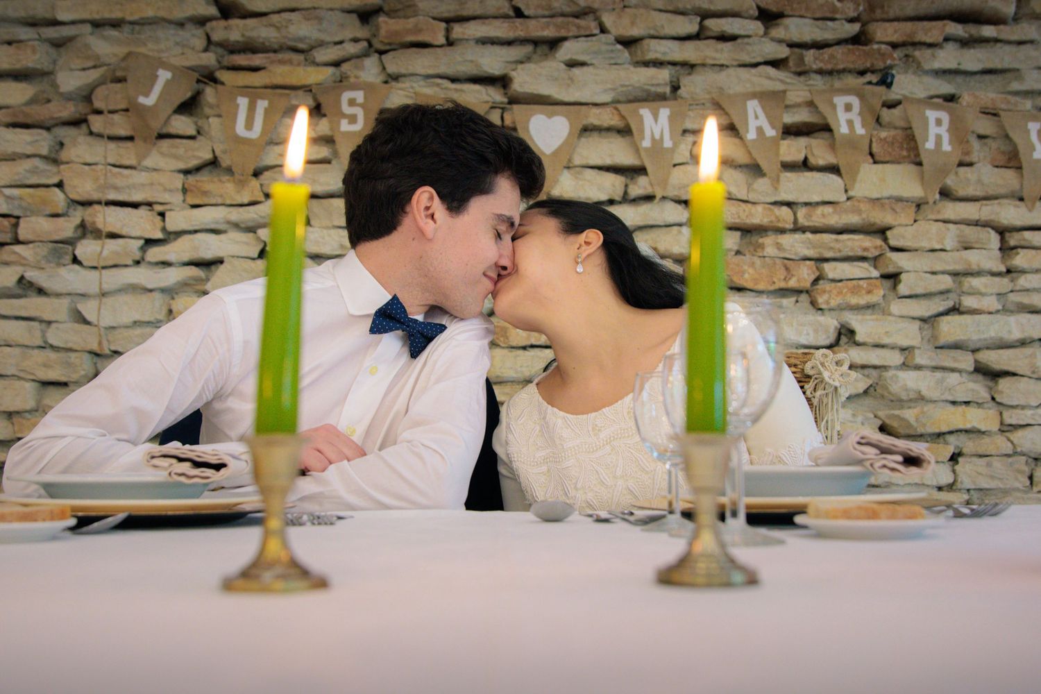 Romantic candlelit dinner scene with stone wall backdrop and green candles on table.