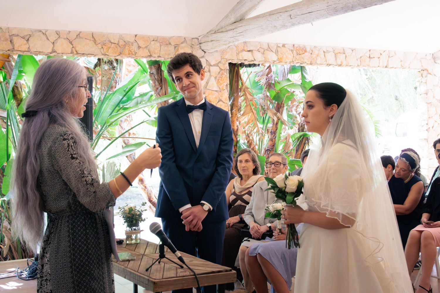 Wedding reception gathering under white tent with tropical greenery decorations.