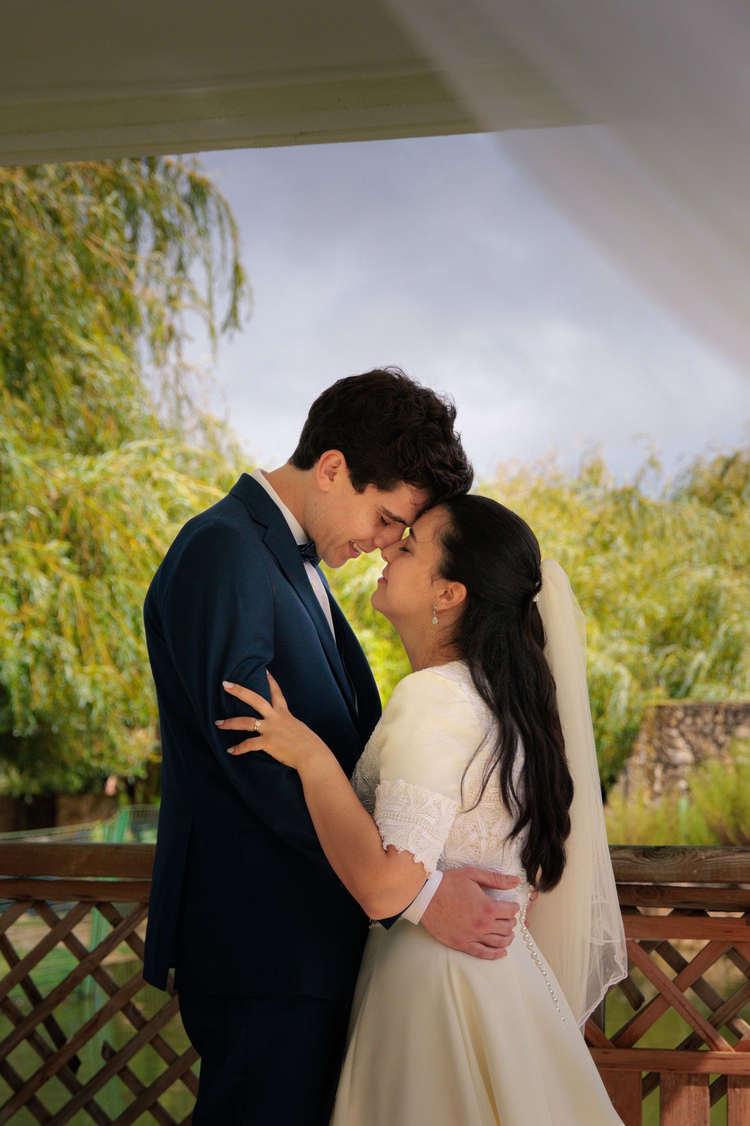 A romantic wedding photoshoot of a couple in formal attire against a natural outdoor backdrop.