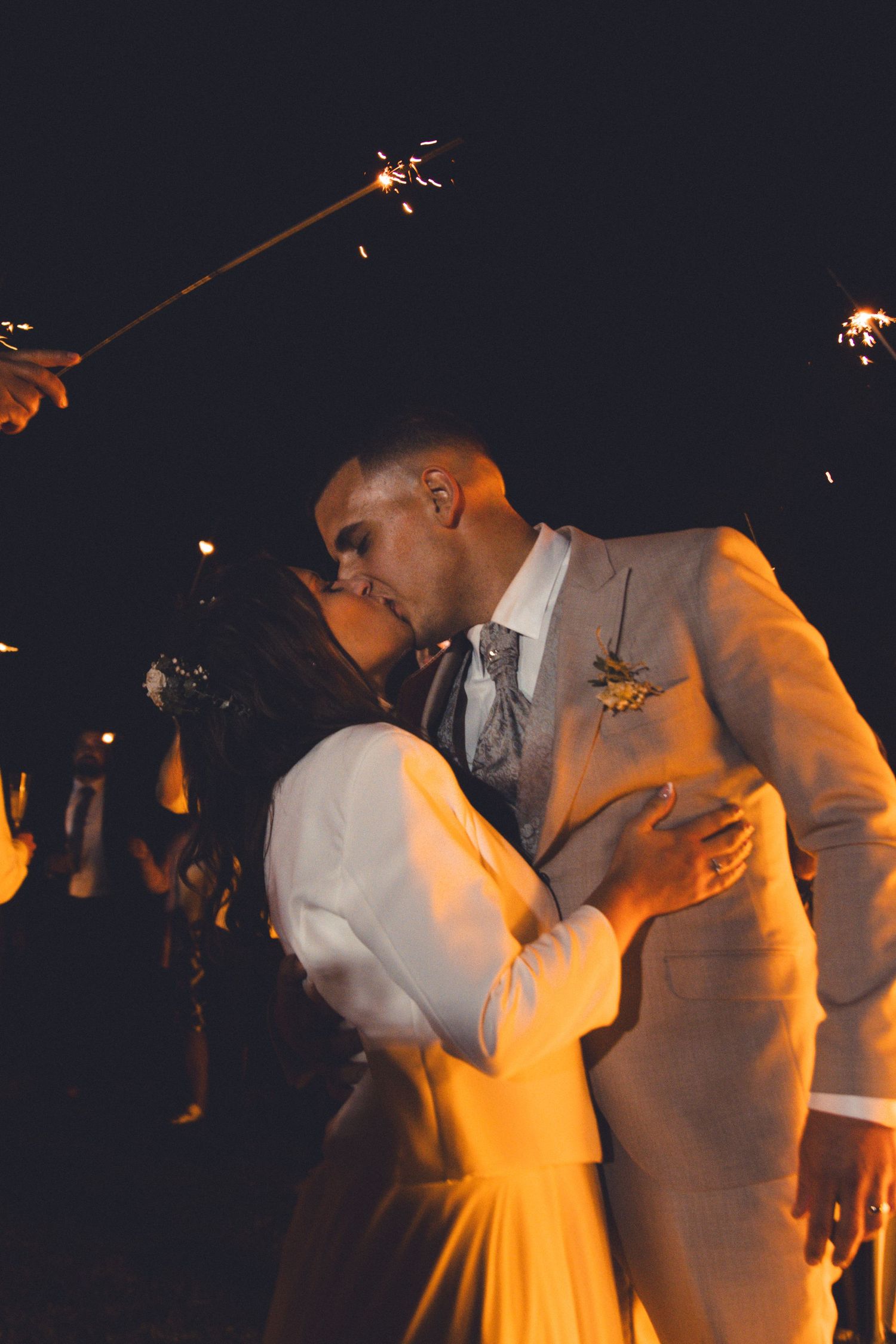 Romantic sparkler kiss between newlyweds during evening wedding reception.