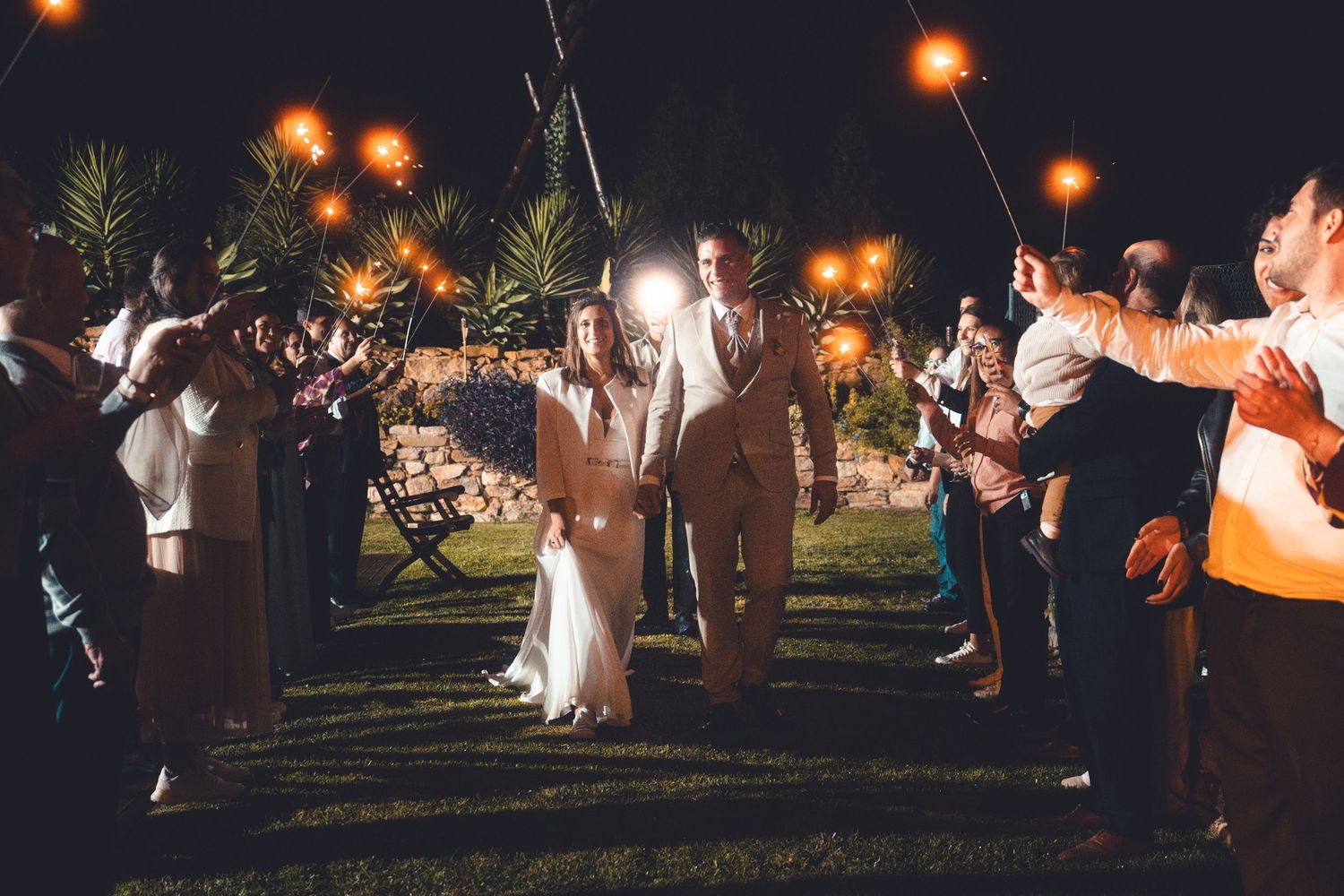 Wedding couple walking through sparkler exit tunnel at night with guests cheering.
