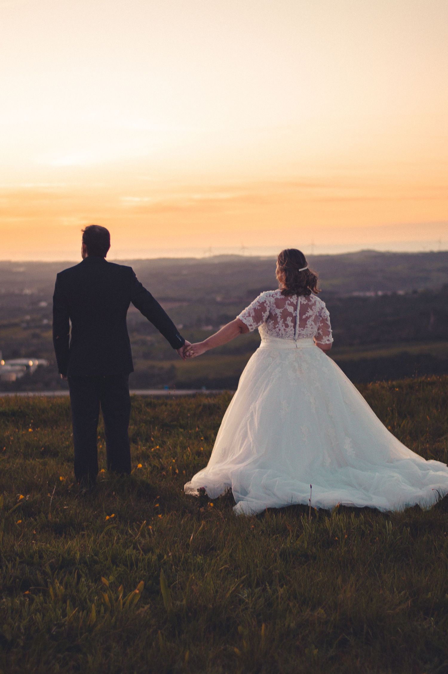 Newlyweds holding hands while standing in field during golden hour.