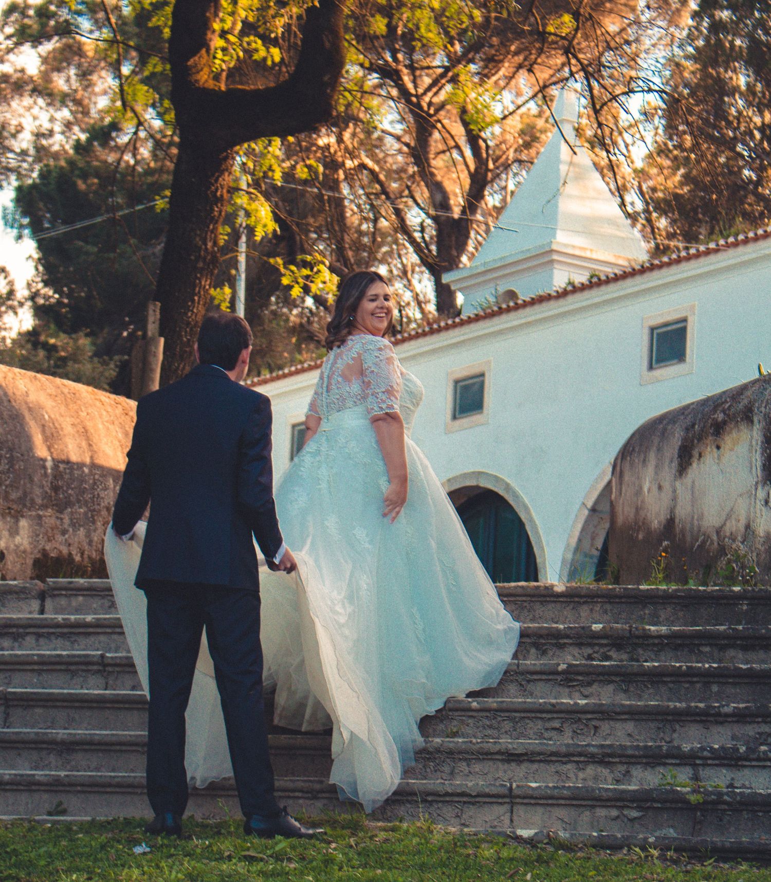 Couple ascending white stone steps near historic building with autumn trees.