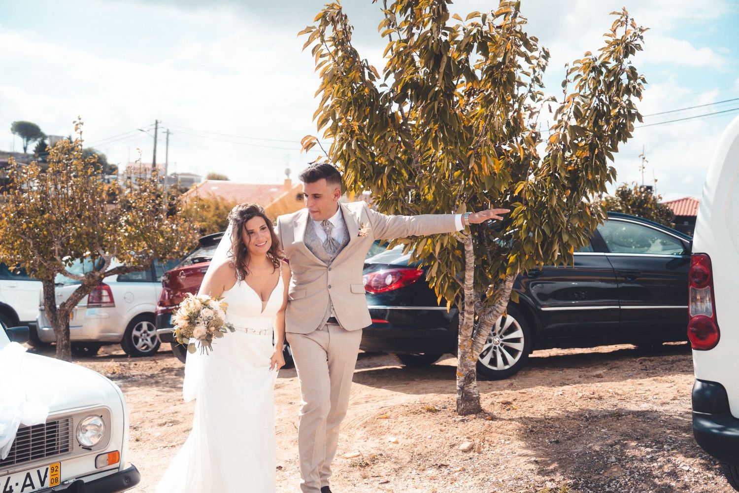 Bride and groom walking hand in hand through outdoor parking area.