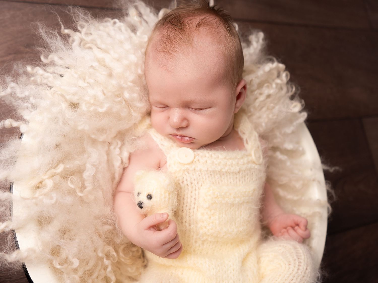 Newborn baby boy wearing yellow fluffy romper with teddy bear sleeping in a bowl prop at newborn session in Doncaster.