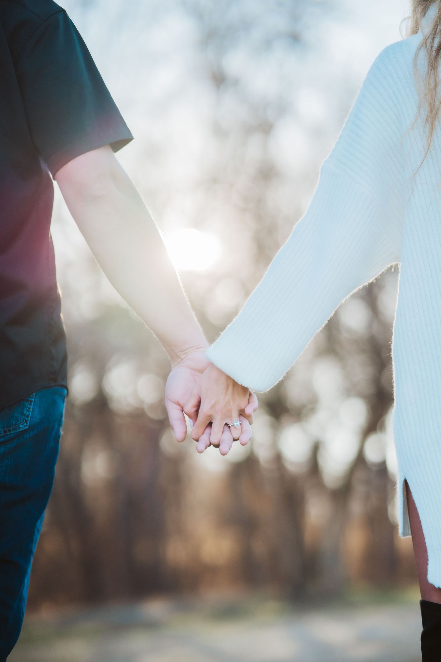 Close-up shot of two people holding hands in sunlit outdoor setting with bokeh background.