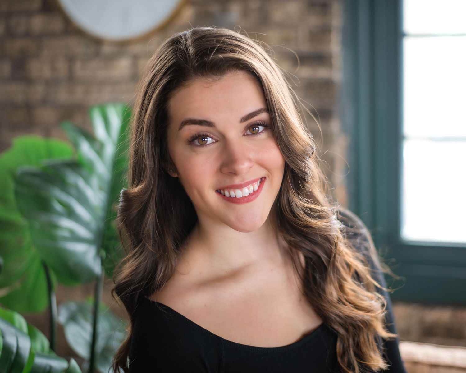 Portrait of person in black top against brick wall with indoor plants.