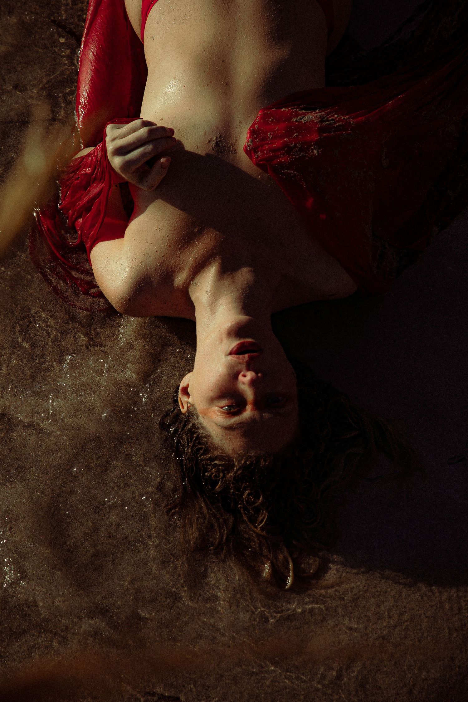 Artistic portrait series of a person in red dress lying on dark textured floor with dramatic shadows and lighting.