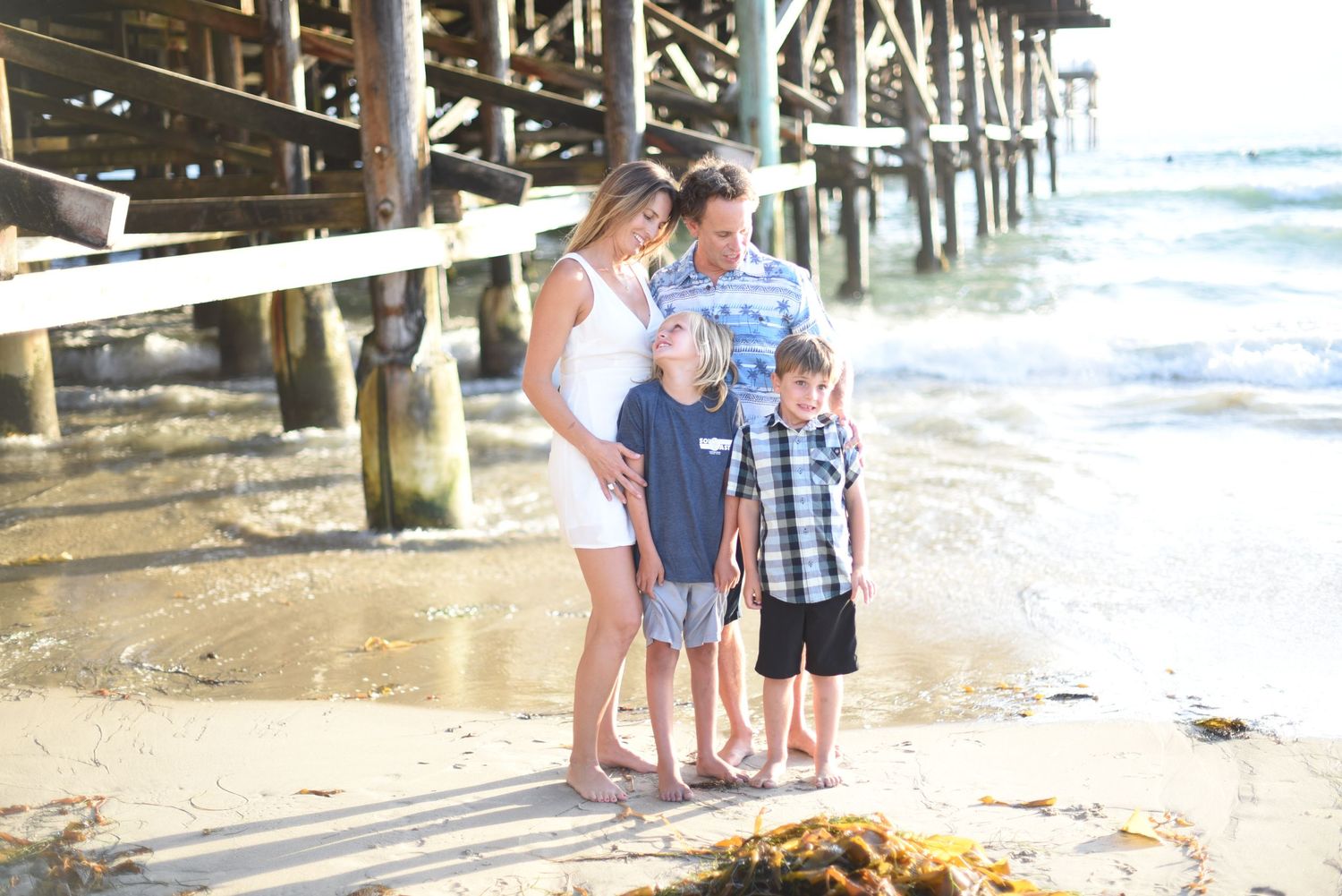 Family enjoying time together under wooden pier at beach during sunset.