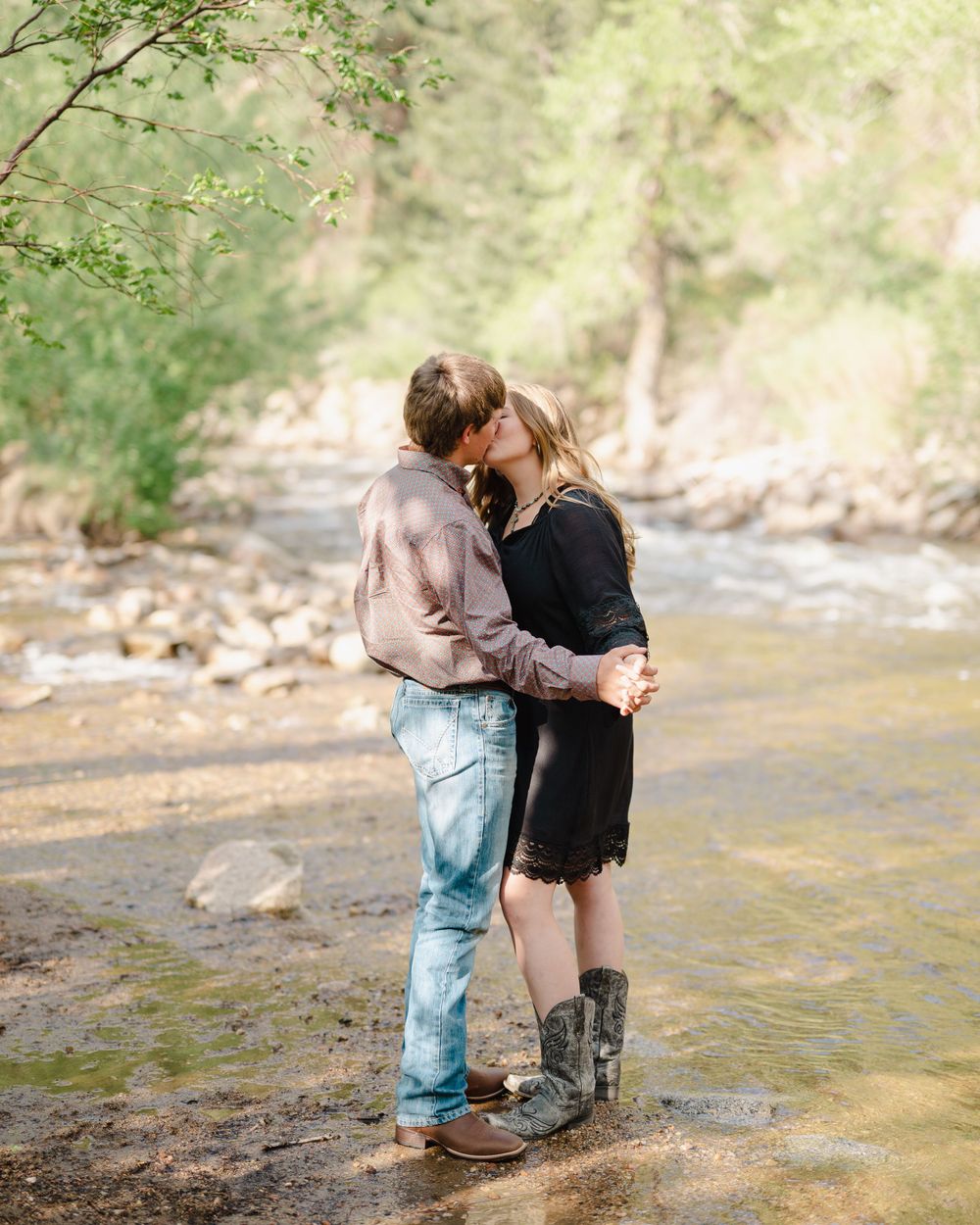 A romantic couple embraces while standing in a shallow creek surrounded by nature.