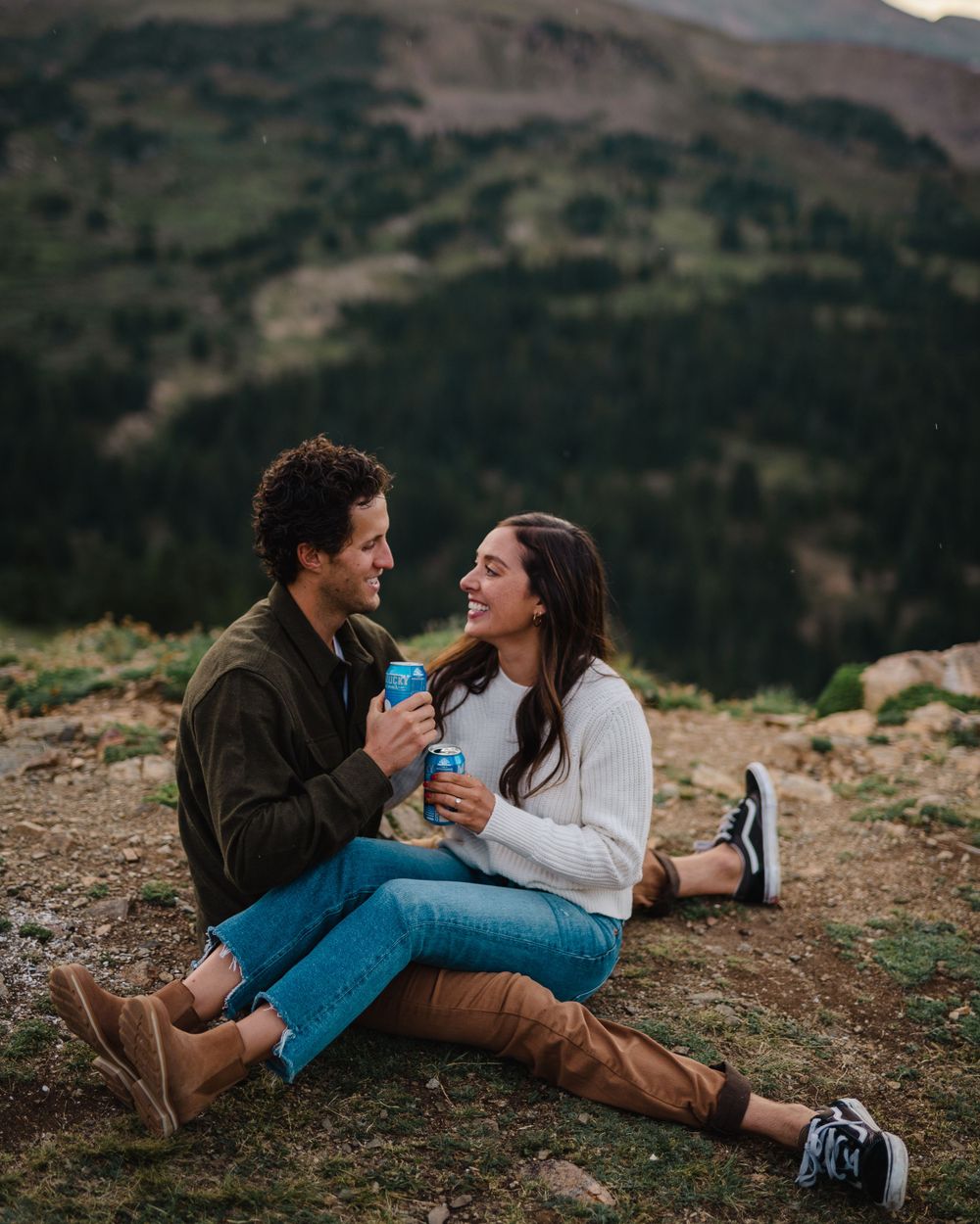 Couple enjoying drinks while relaxing on a mountainside during sunset.