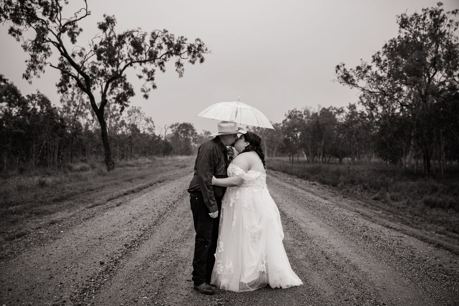 Black and white photo of couple with umbrella on rainy country road.