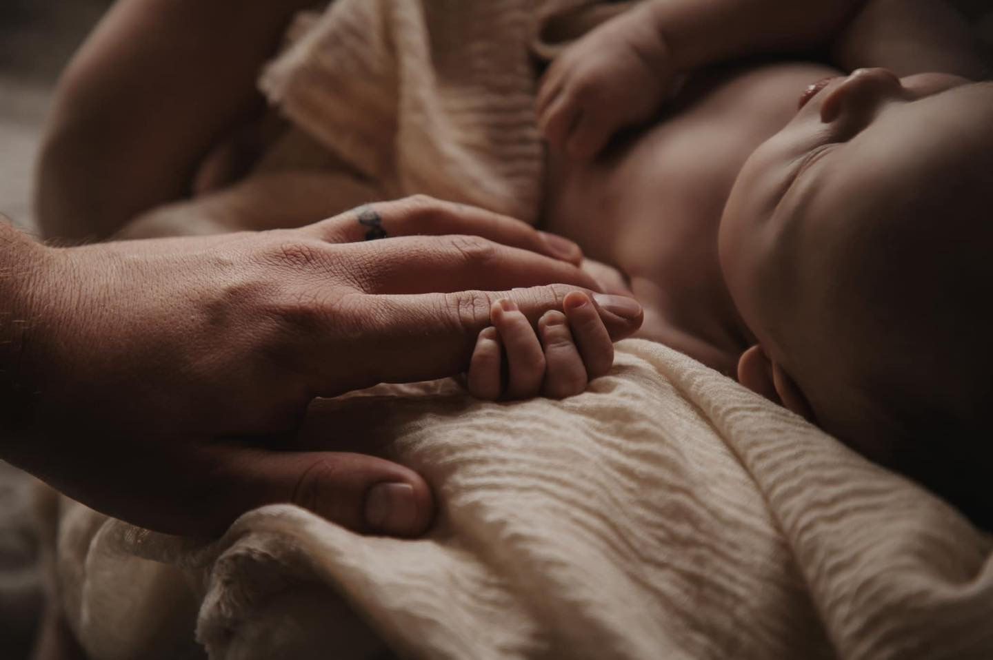 A tender moment captured as hands touch on soft fabric in gentle lighting.