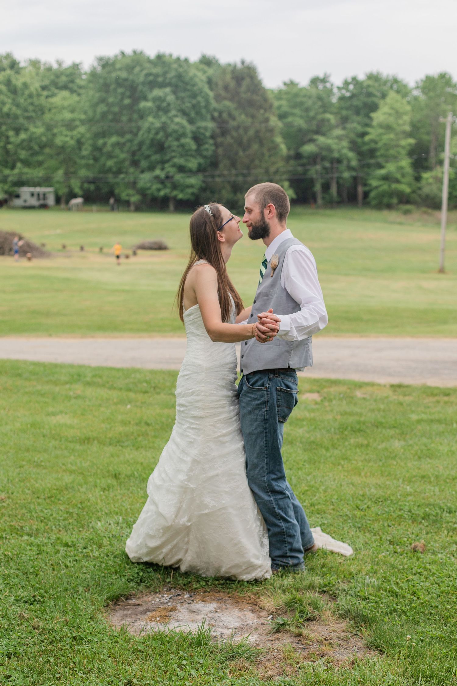 Couple dances playfully on grass during their rustic outdoor wedding celebration.