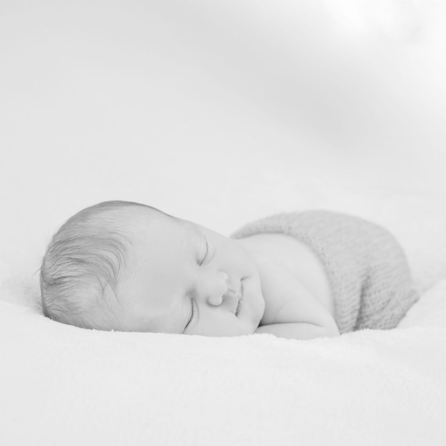 black and white baby sleeping while smiling peacefully on a soft fluffy blanket for a newborn photo shoot