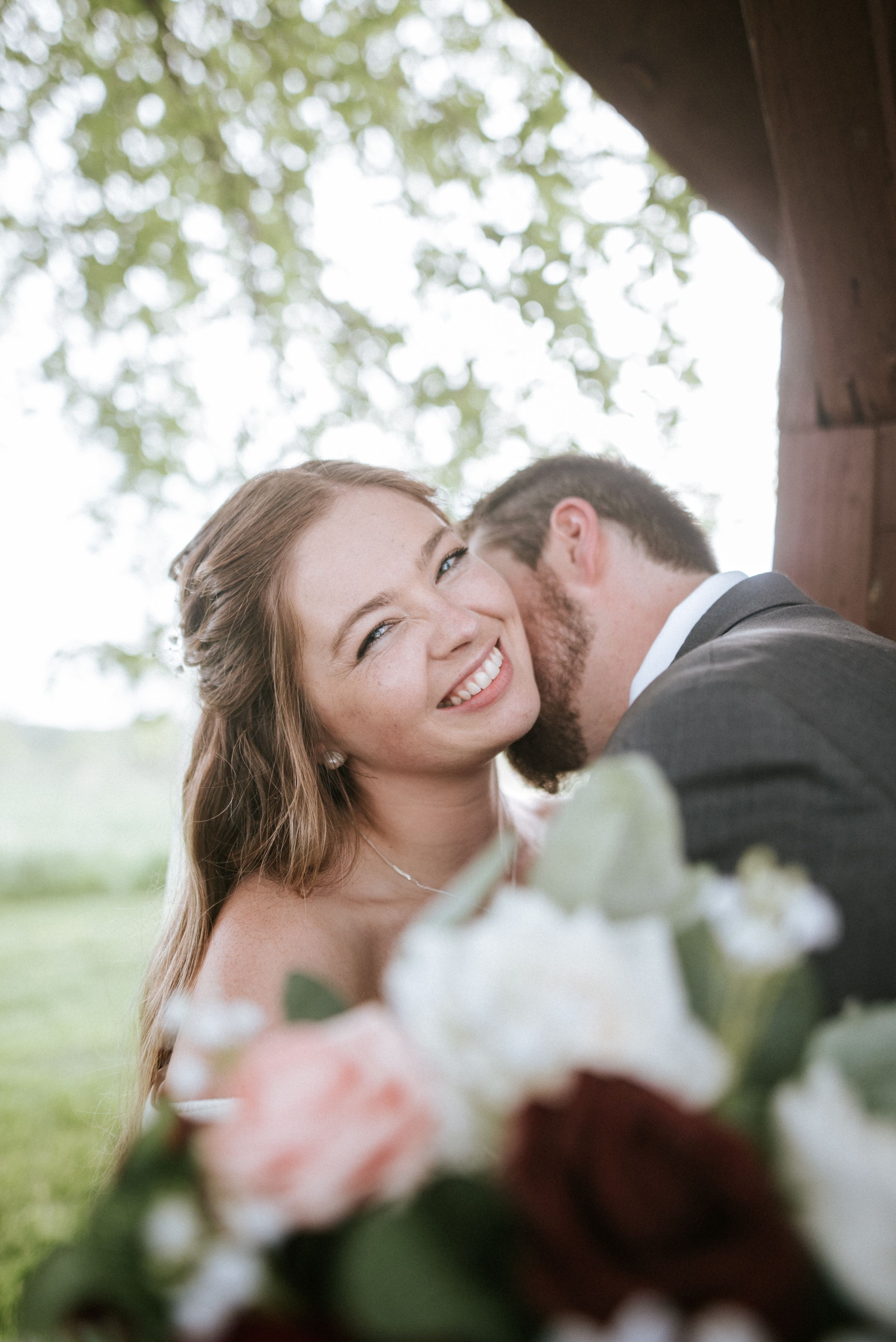 A joyful moment captured between newlyweds with a bouquet of roses in natural outdoor lighting.