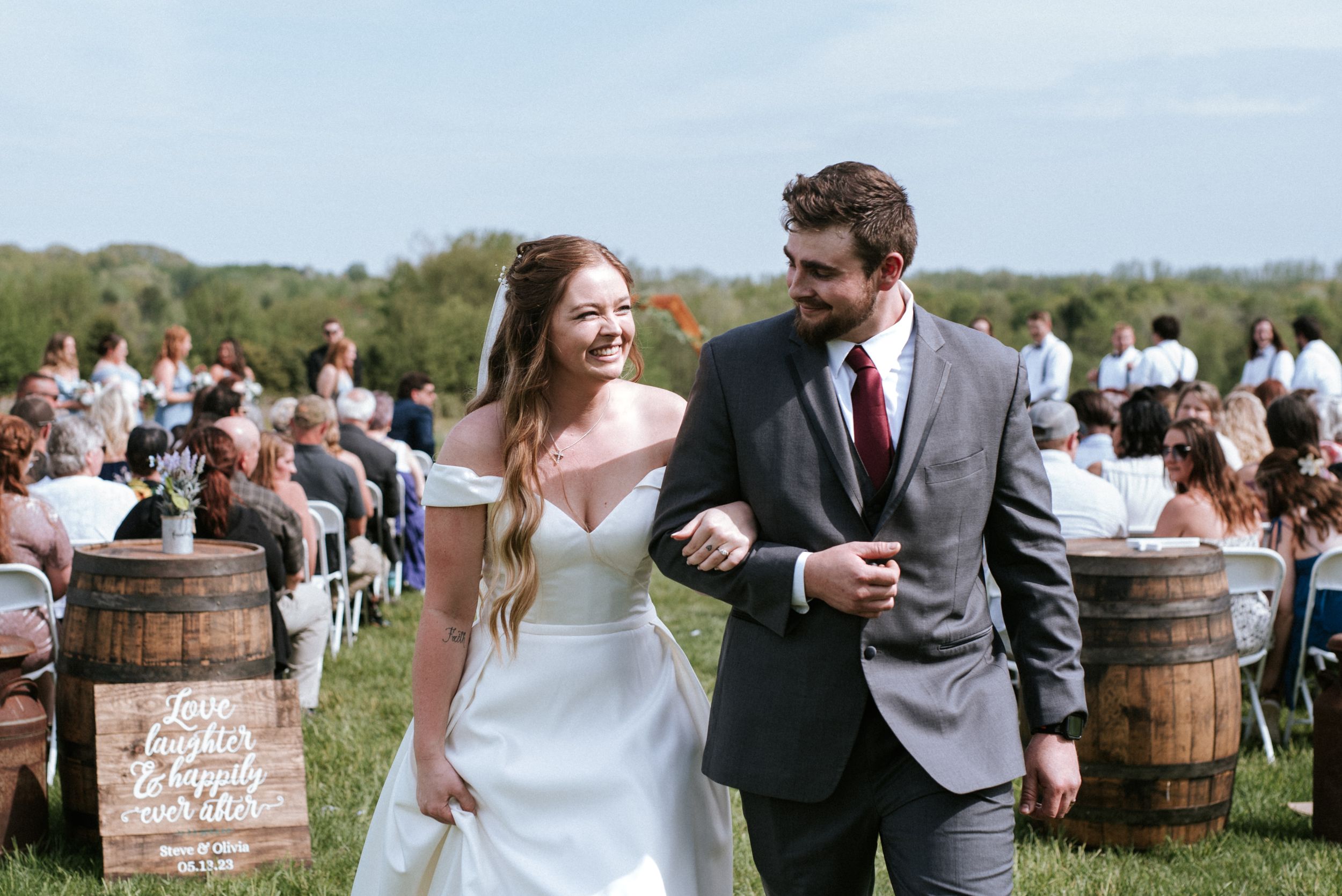 Wedding couple walking between wine barrels at outdoor ceremony venue.
