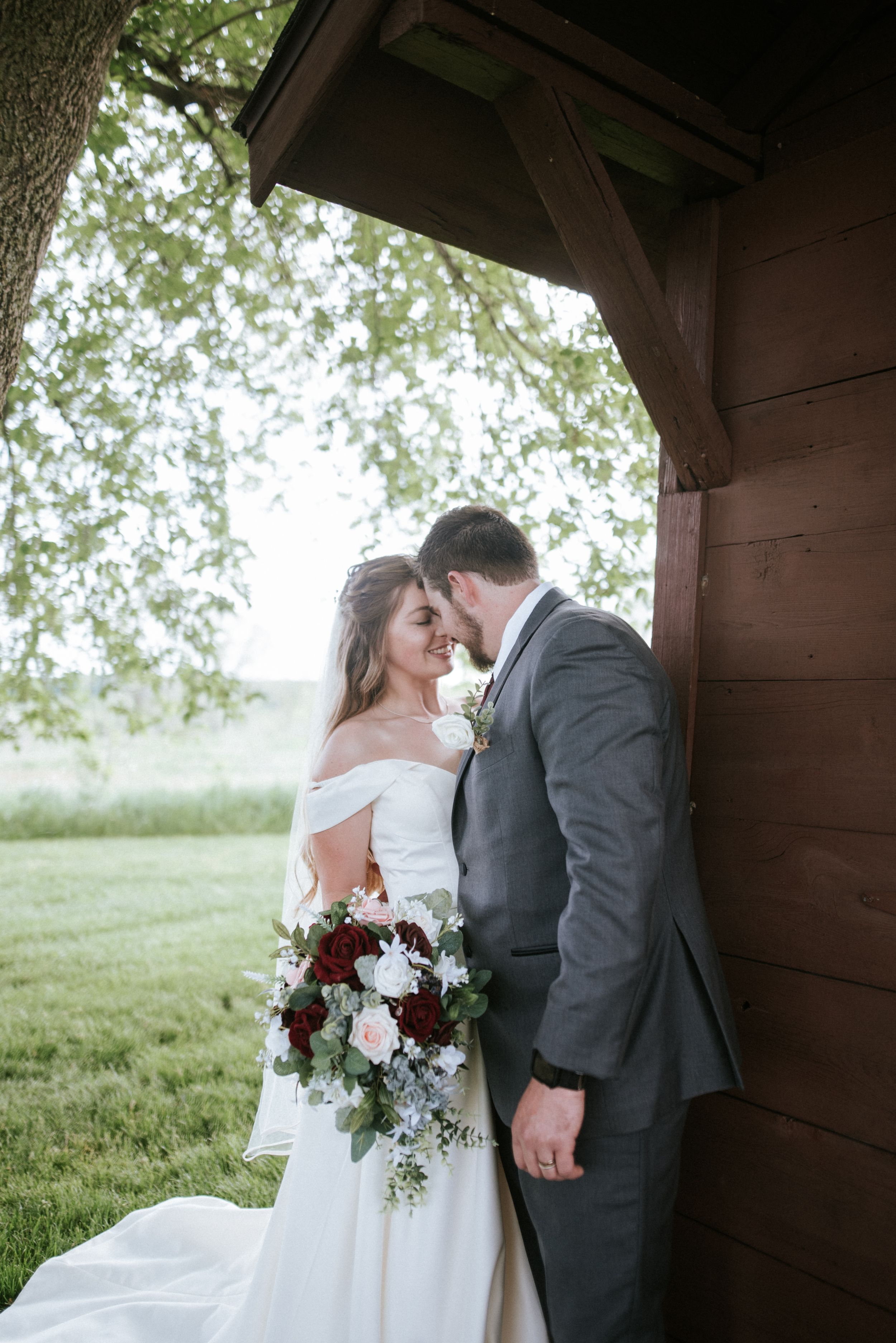 A romantic wedding portrait of a couple sharing an intimate moment against a rustic wooden barn.