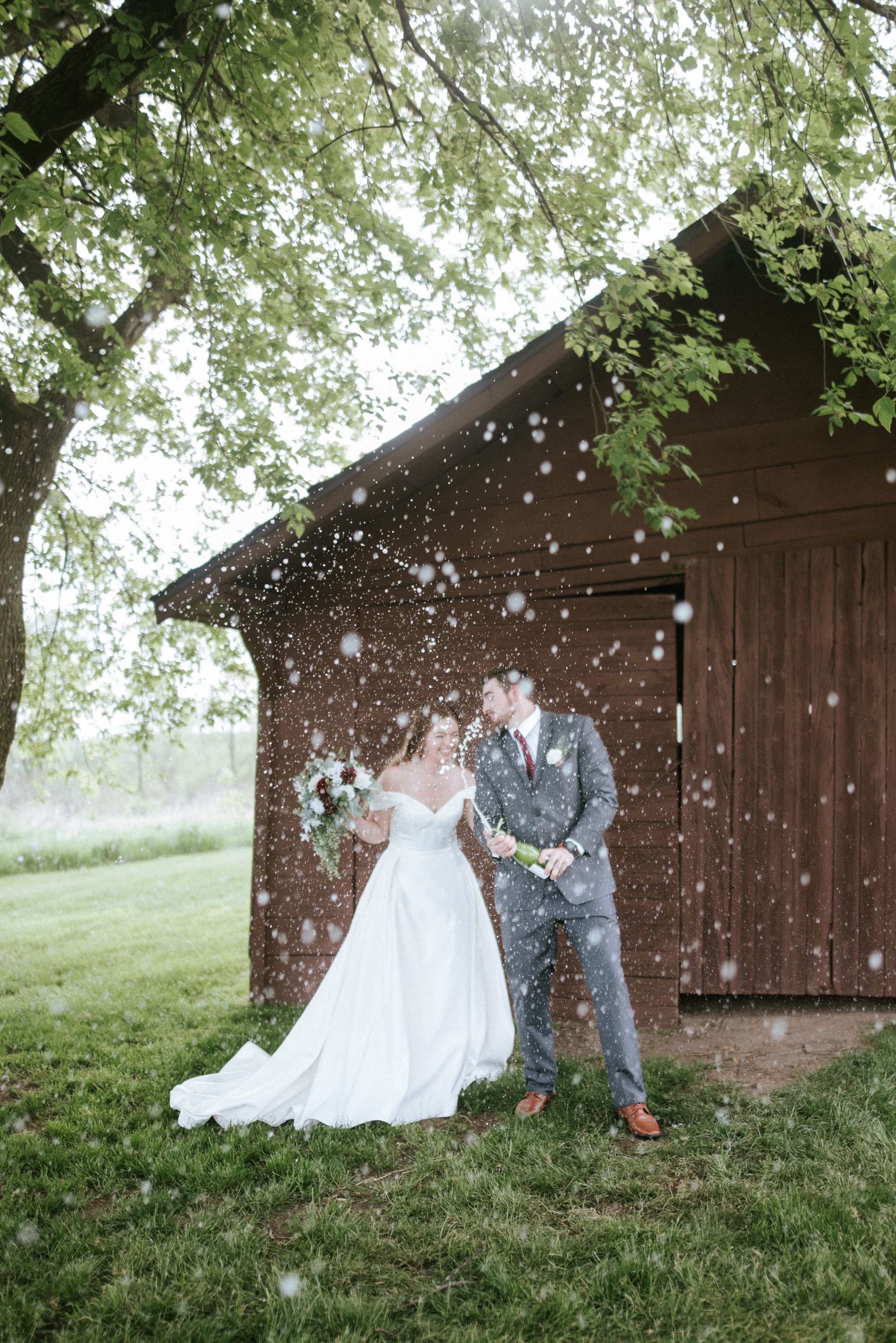 A wedding couple stands by a rustic barn while confetti falls around them in a dreamy outdoor setting.