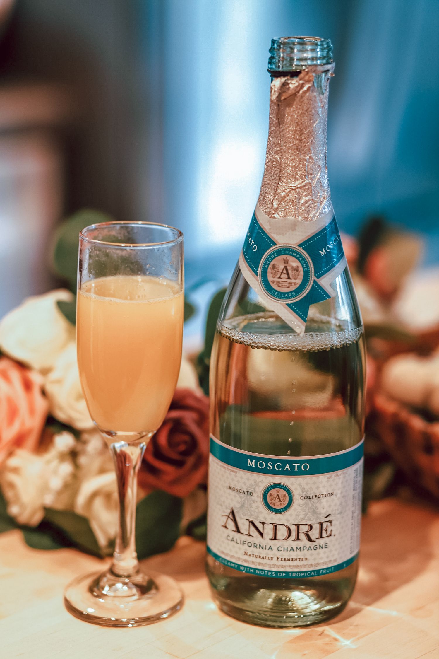 Bottle of Andre Moscato champagne with filled mimosa glass on decorated table.