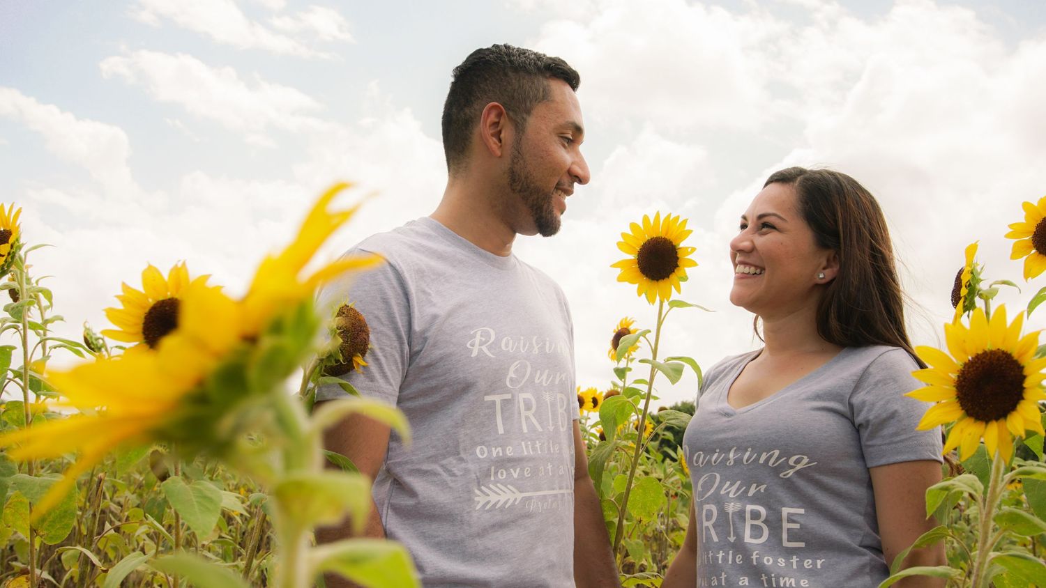 Happy couple in matching gray shirts smiling at each other in a vibrant sunflower field.