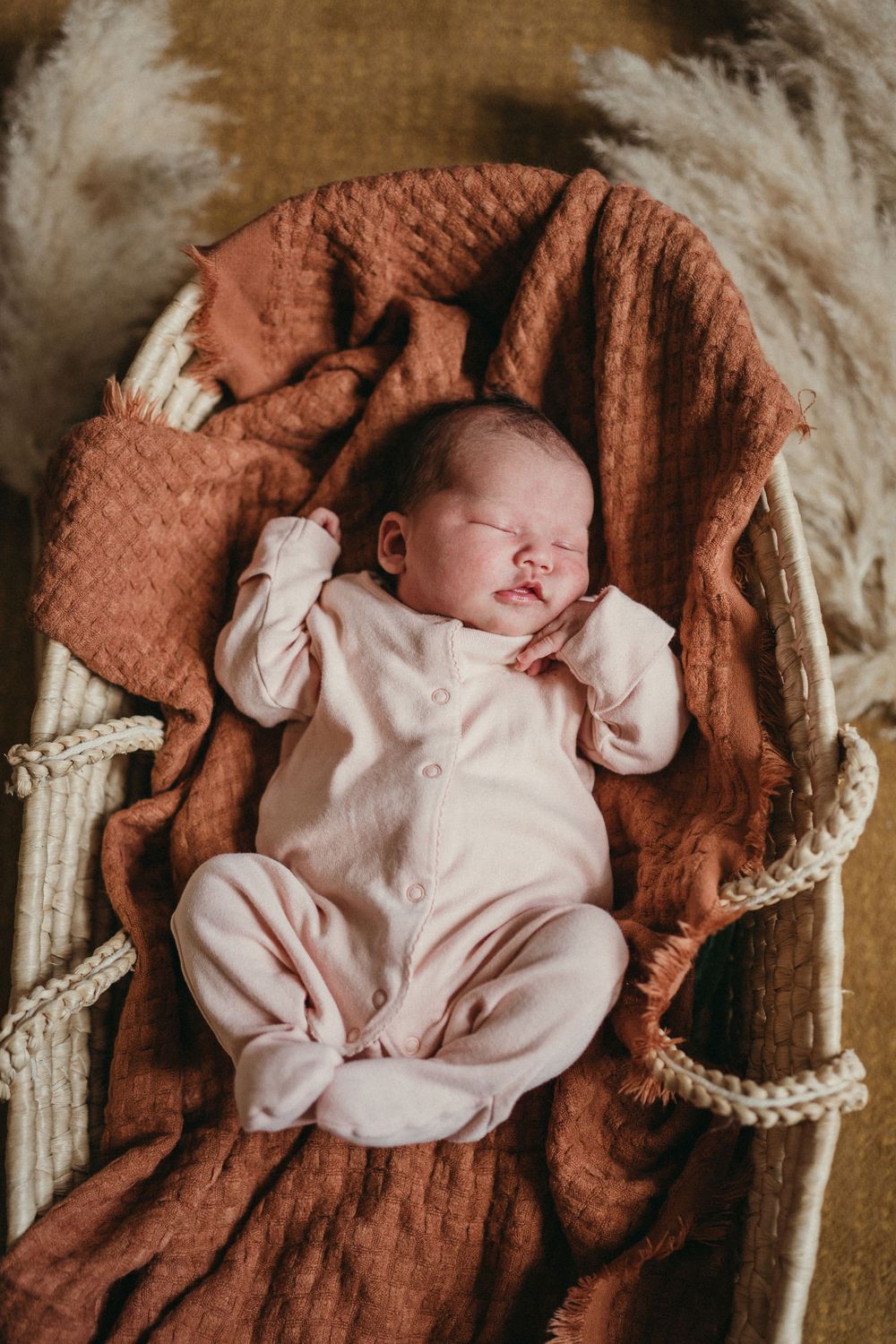 newborn baby laying on a orange blanket in a comfy moses basket